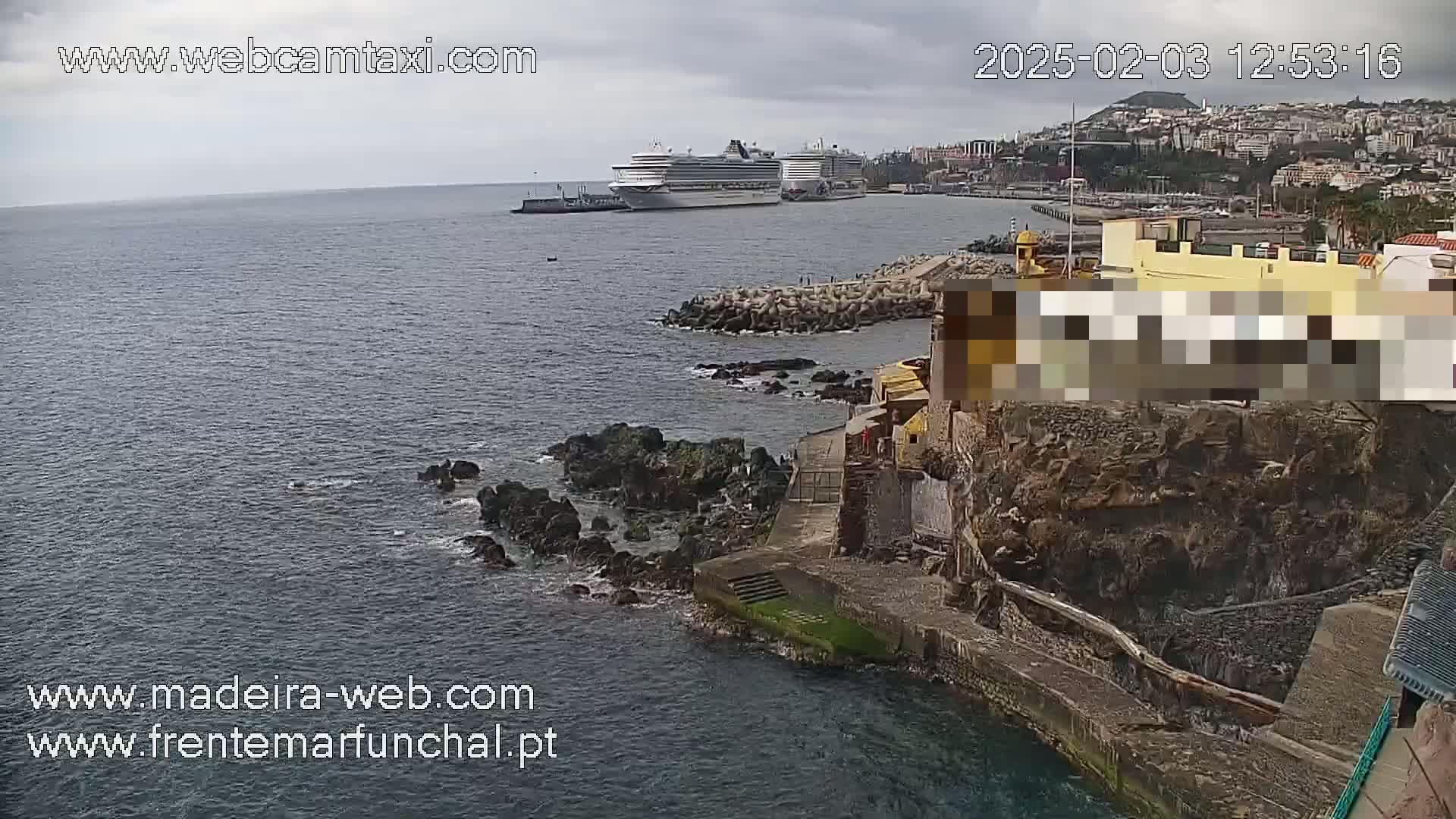 A cruise ship is docked near a rocky shoreline in a harbor under overcast skies.