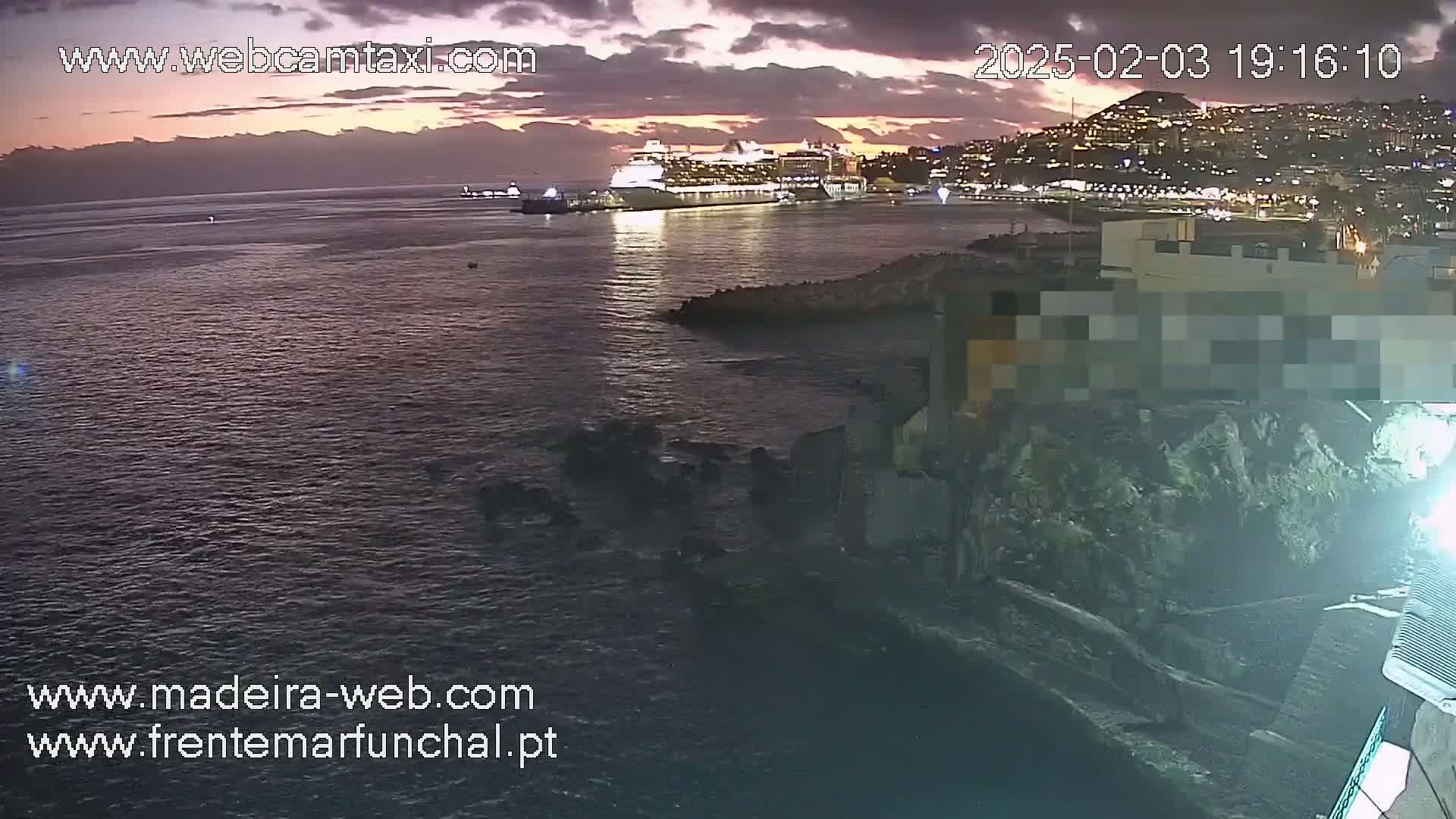 A large cruise ship is docked near a city at twilight under a partly cloudy sky.