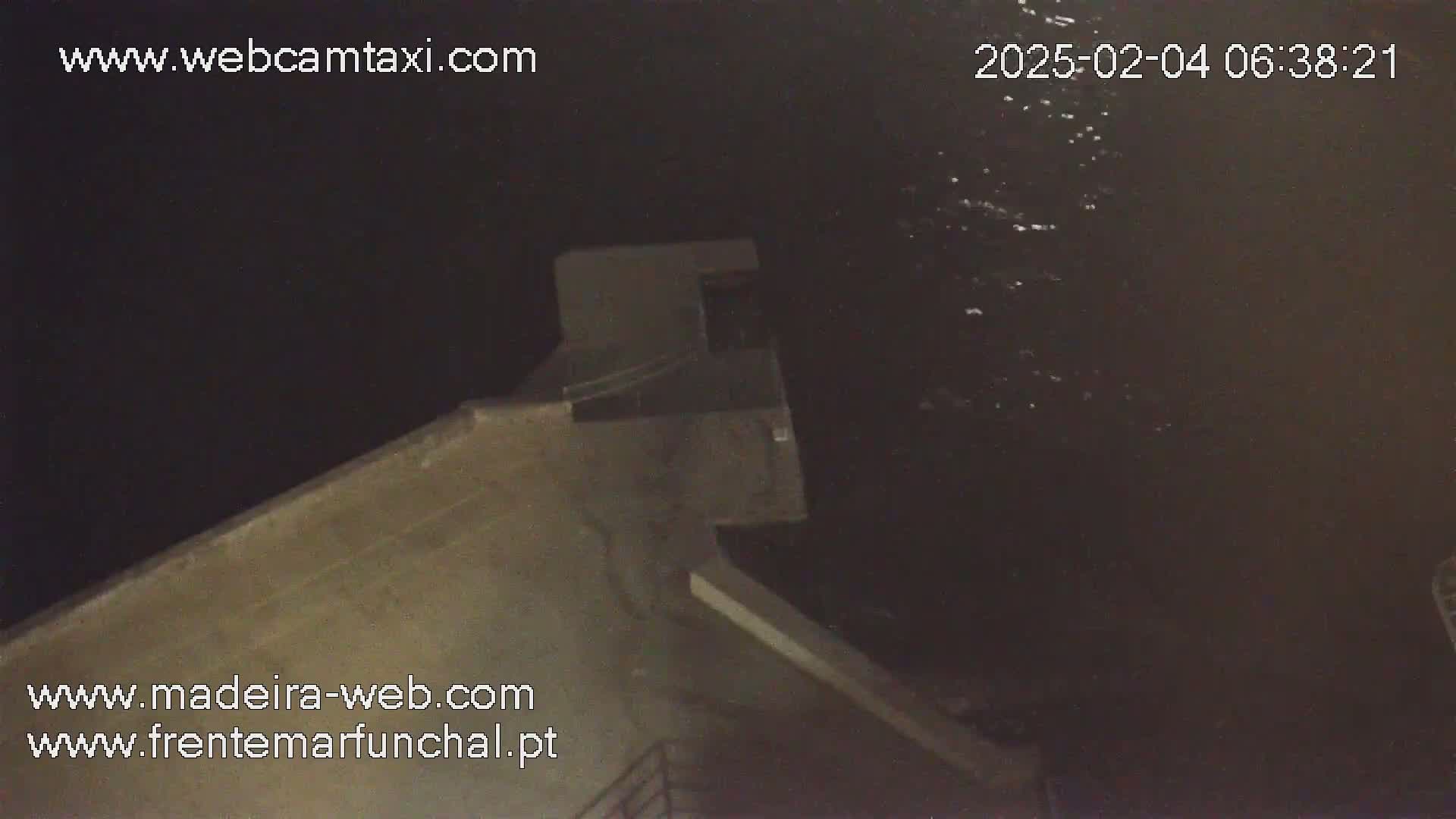 A nighttime, high-angle view shows a section of a concrete structure extending into dark, slightly wavy water.