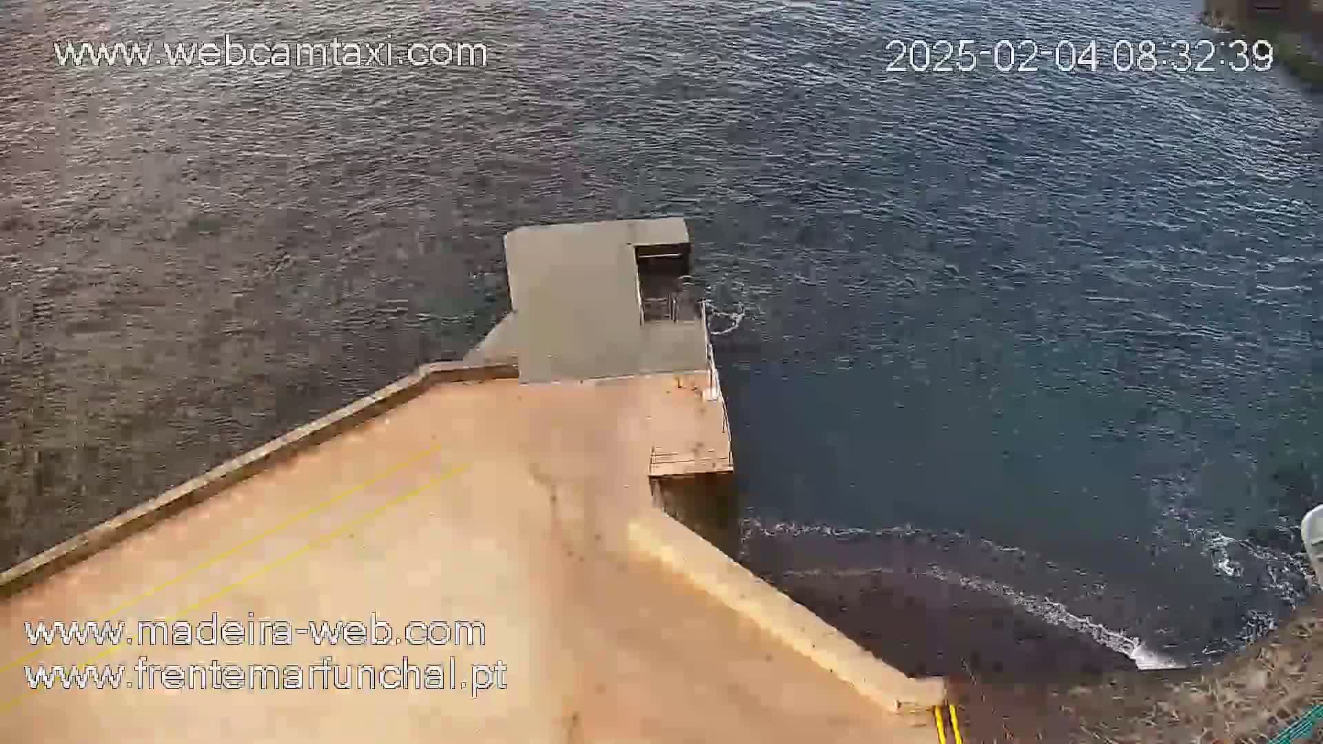 An aerial view shows dark water flowing near a concrete structure on a calm day.
