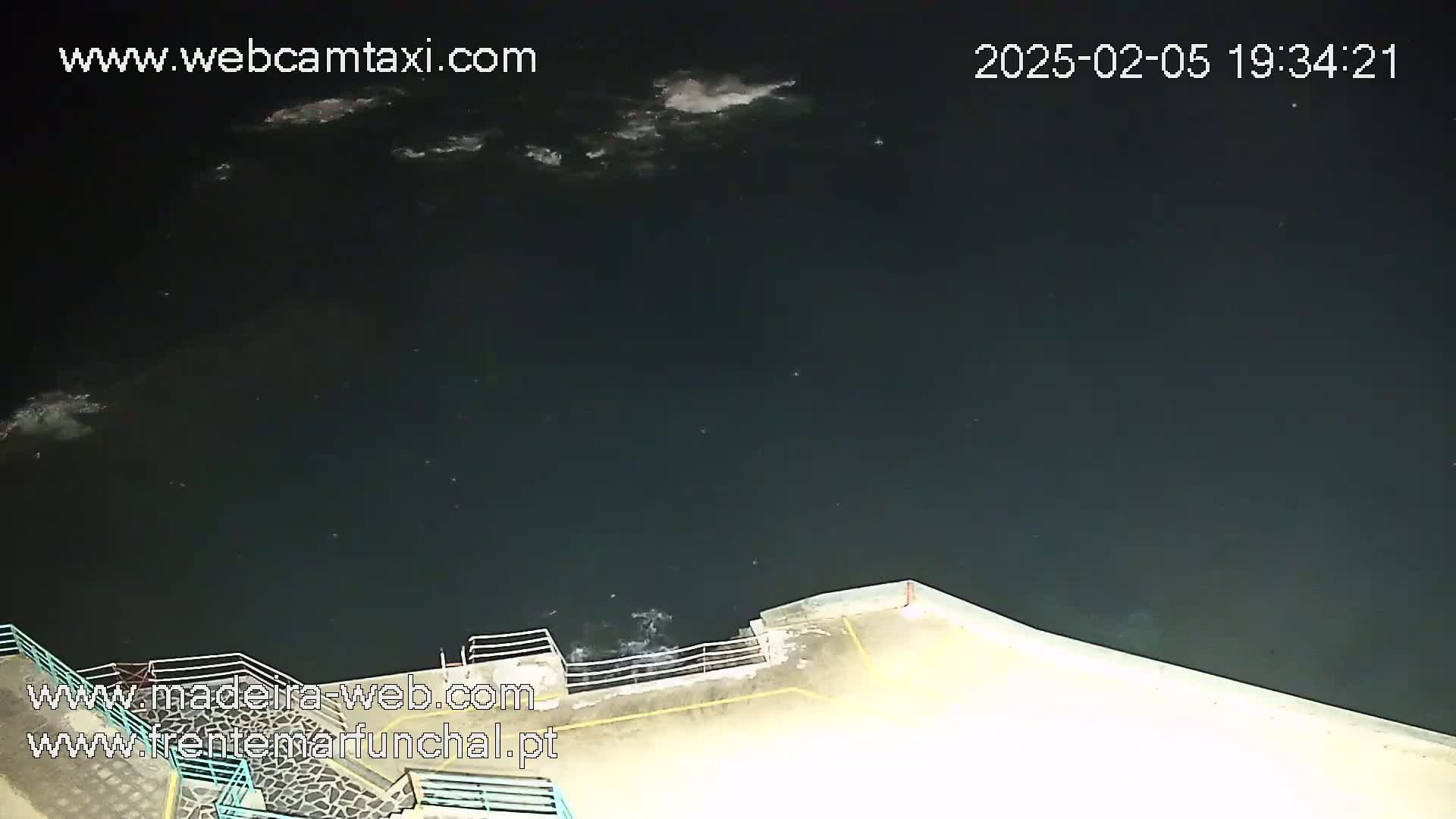 A nighttime, high-angle view shows dark water with some small waves lapping against a concrete seawall.