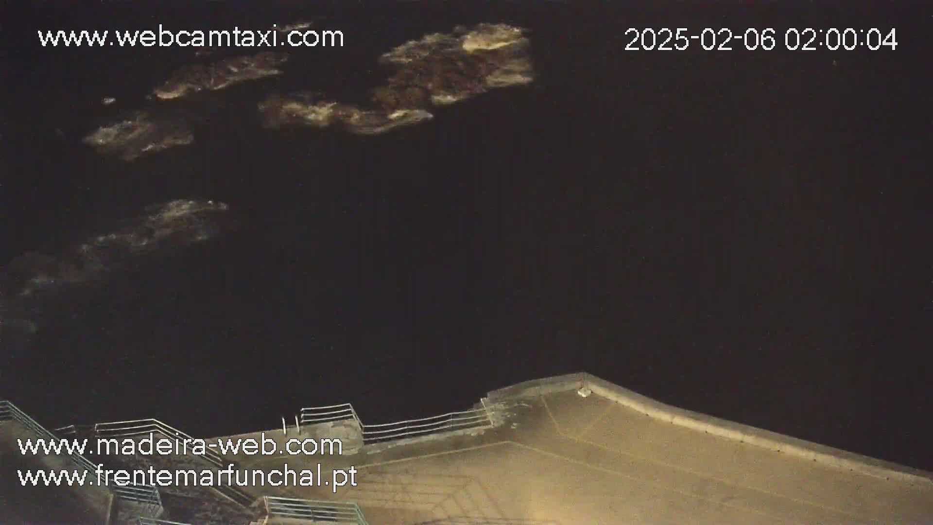A nighttime, dark-water view shows faintly illuminated waves and a portion of a concrete structure with a railing.