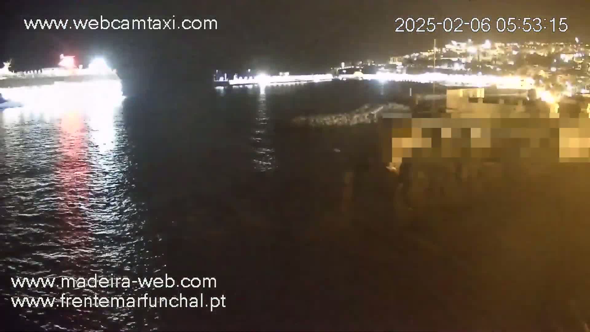 A large ship is docked at a brightly lit waterfront at night, with calm water reflecting the lights.