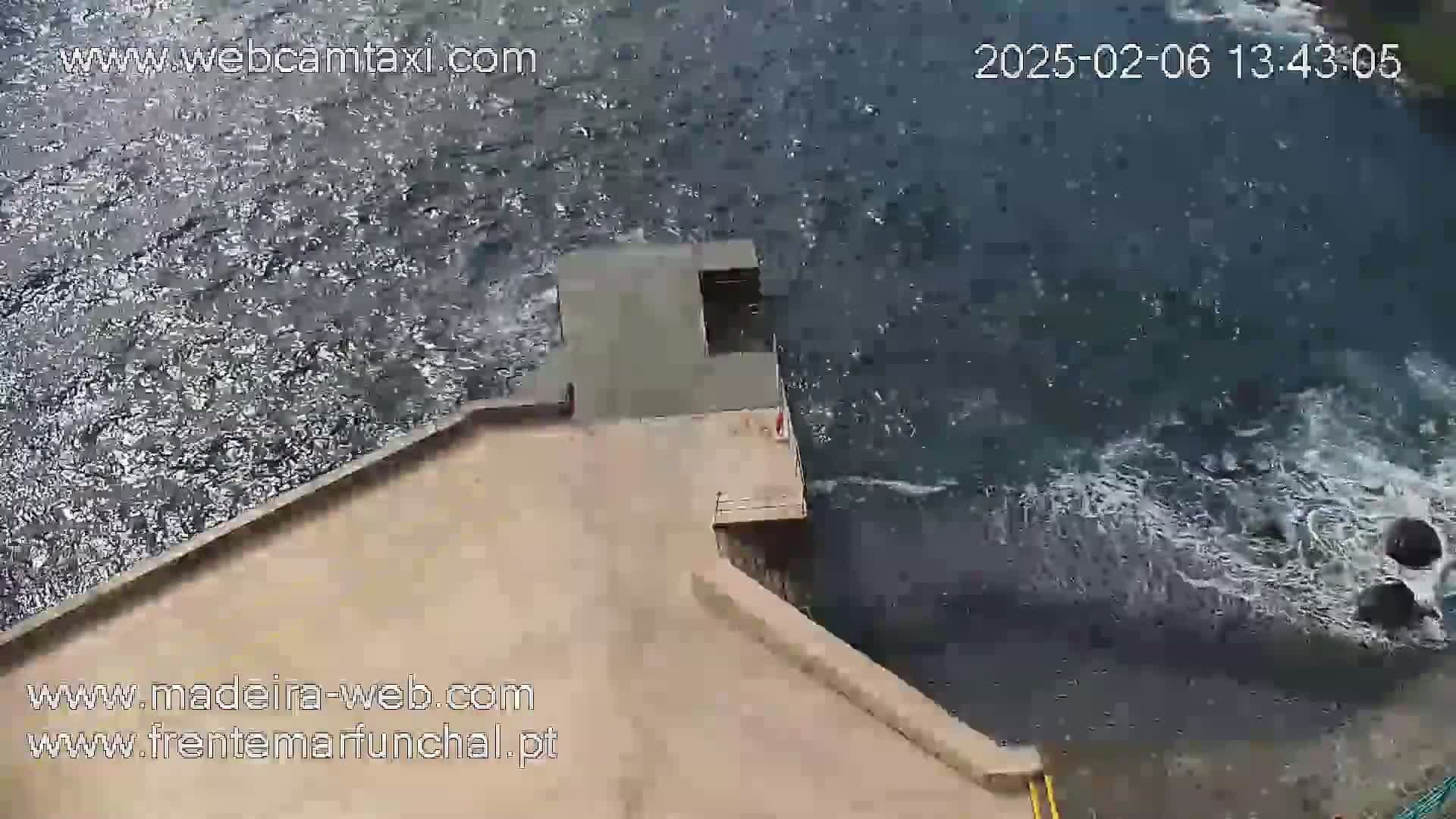 An aerial view shows a concrete platform extending over choppy dark water.