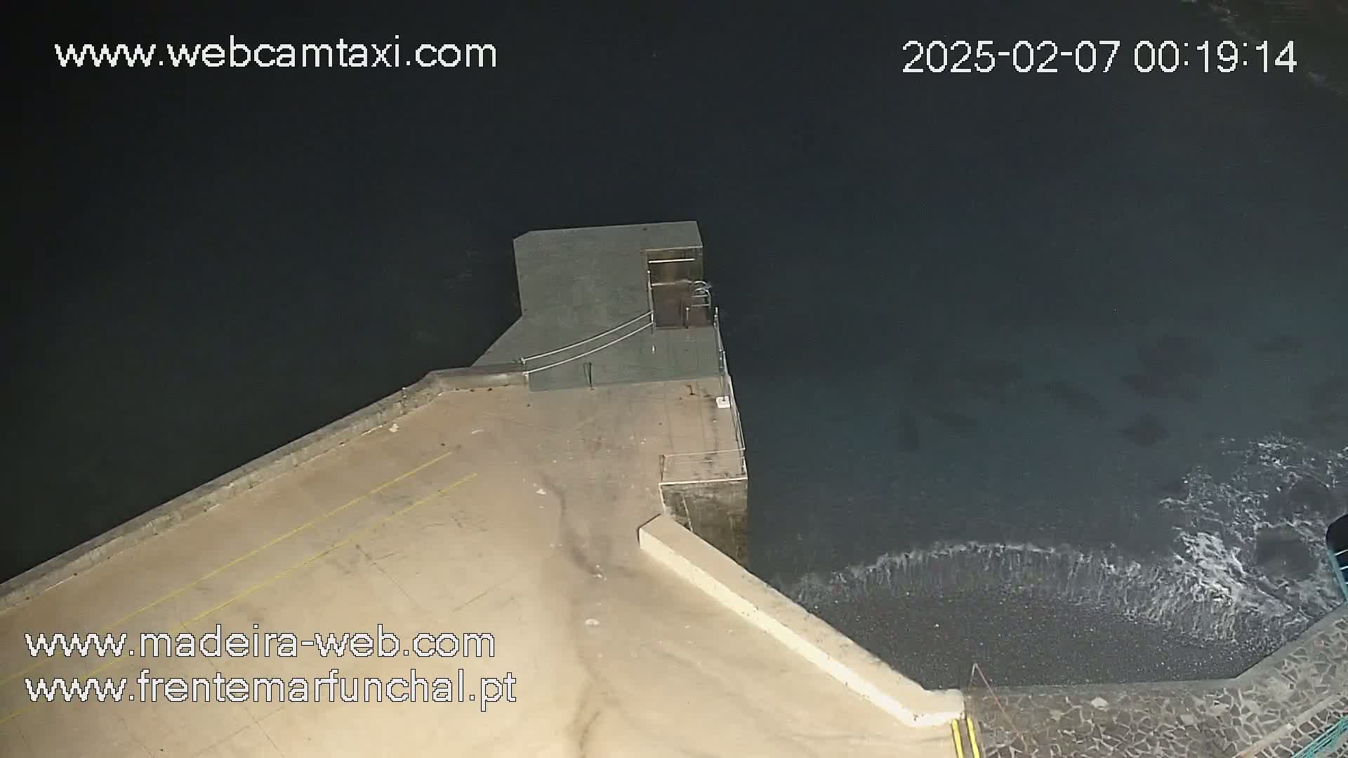 A nighttime, high-angle view shows a dark-colored body of water lapping against a concrete structure, with small waves visible near the shore.