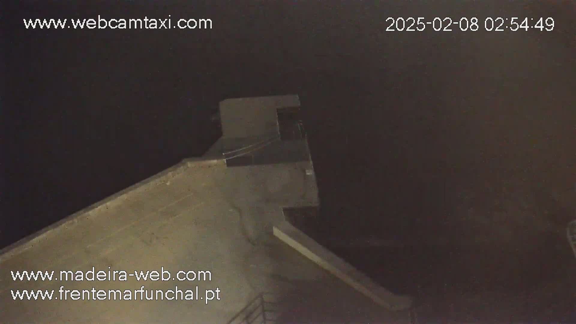 A nighttime, high-angle view shows a portion of a concrete structure, possibly a rooftop or embankment, under a dark sky.