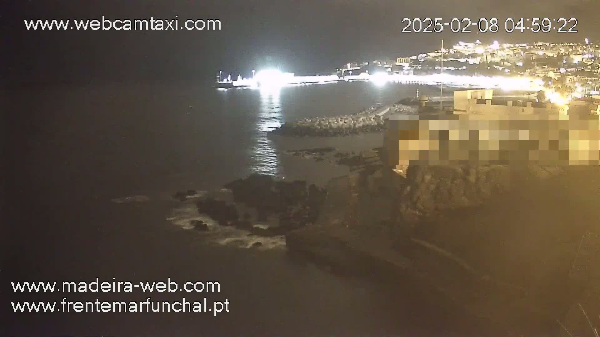 A nighttime view of a harbor with a partially visible building and a ship at the dock, under calm water conditions.