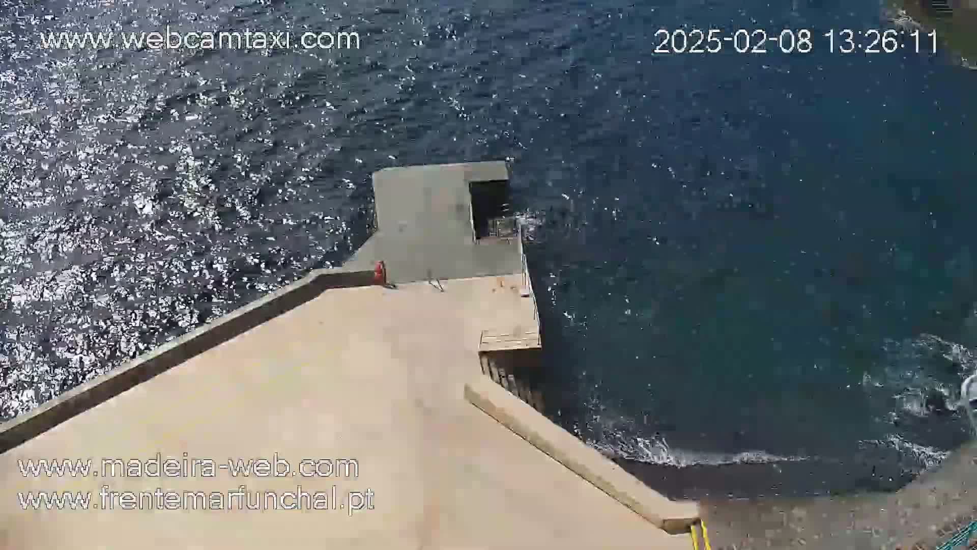 A tan concrete platform meets a dark-blue, slightly wavy ocean under a sunny sky.