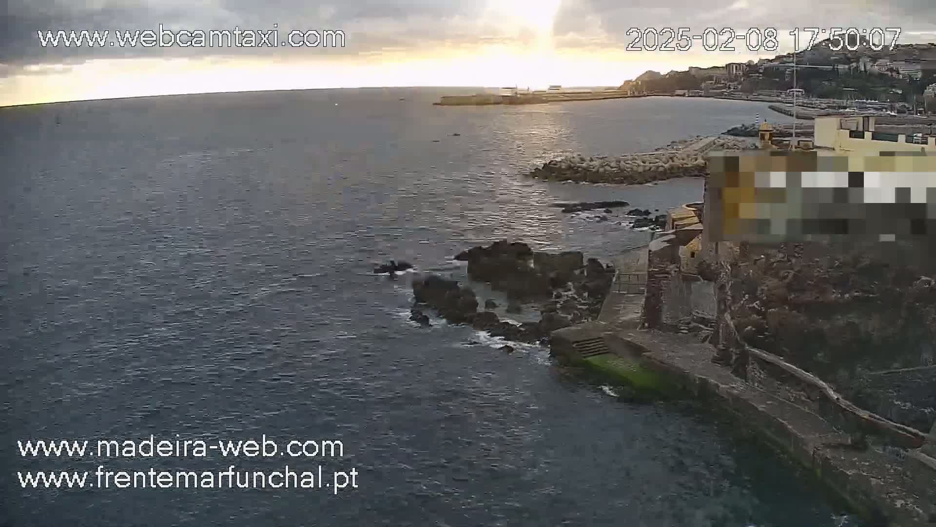 A high-angle, long shot of a rocky coastline at sunset with calm, dark water.