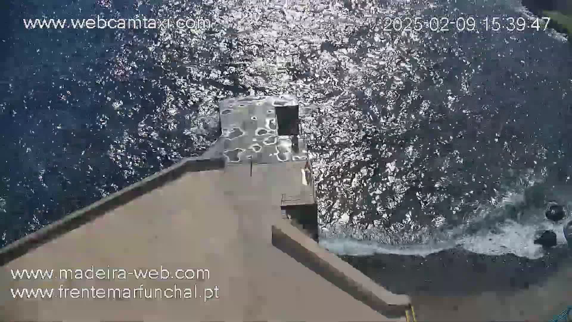 A tan concrete structure extends over dark, choppy water with small waves crashing against it.