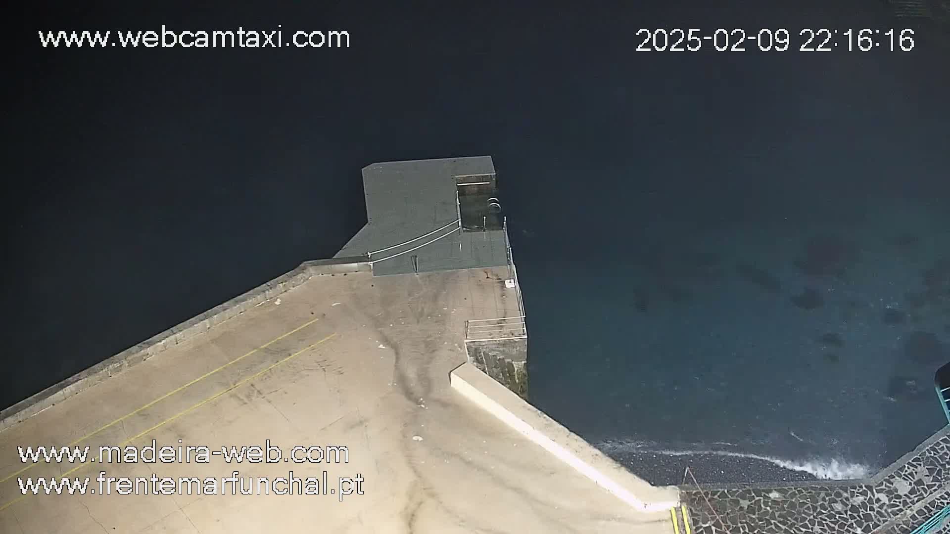 An aerial nighttime view shows a dark-colored body of water lapping against a concrete structure.