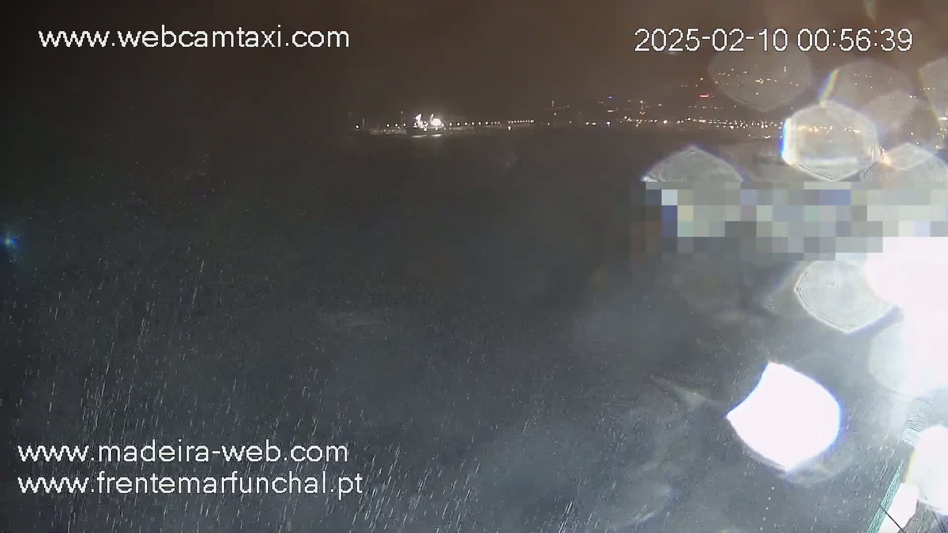 A nighttime, rainy view shows a blurred cityscape in the distance with lights visible along a waterfront.