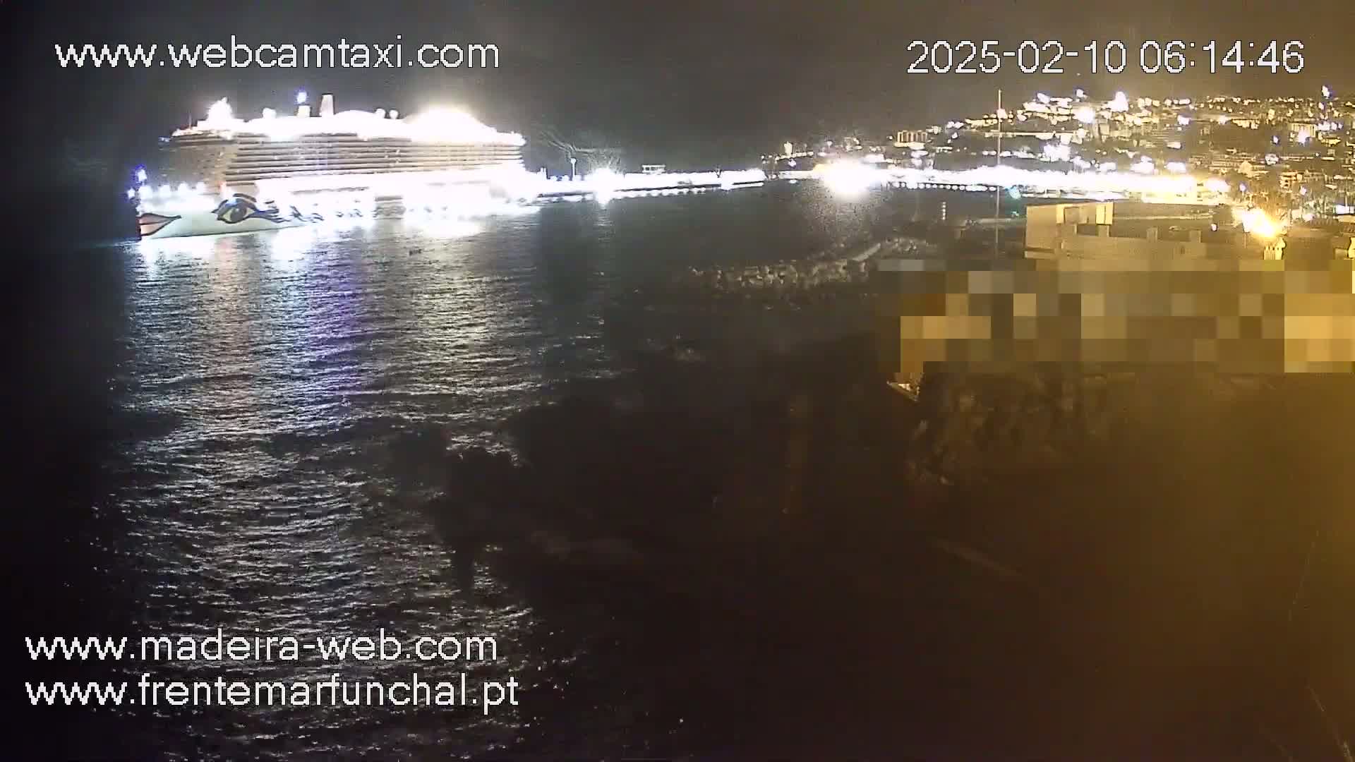 A large cruise ship is docked at a brightly lit waterfront at night, with dark, slightly wavy water surrounding it.