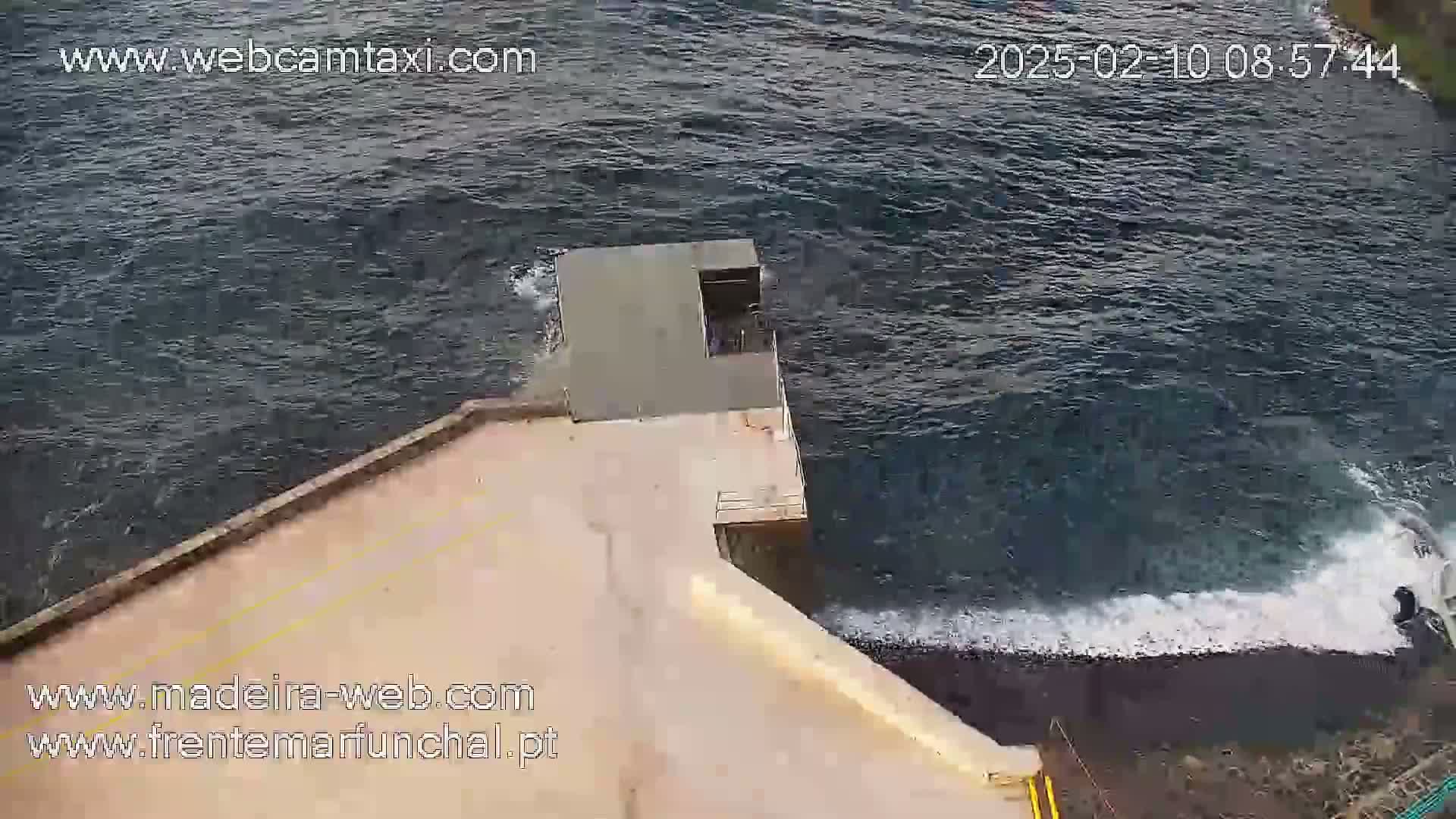 A concrete structure juts out into a dark-blue, choppy ocean with small waves crashing against its edge.