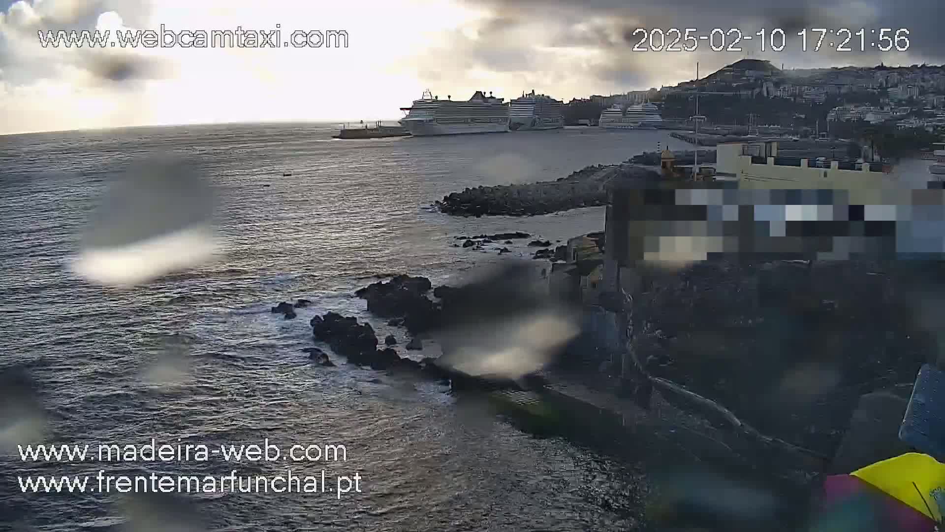 Several cruise ships are docked in a harbor under a partly cloudy sky, with rain visible on the camera lens.