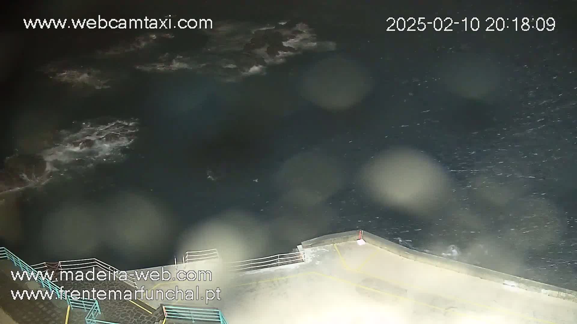 A nighttime, high-angle view shows dark, choppy water lapping against a low seawall.