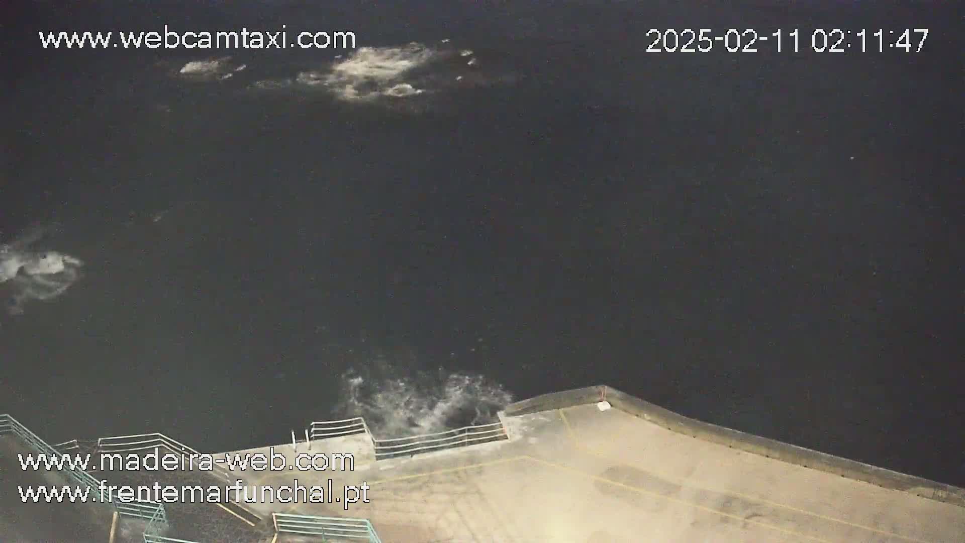 A nighttime view of dark water with small whitecaps near a concrete seawall under a partly cloudy sky.