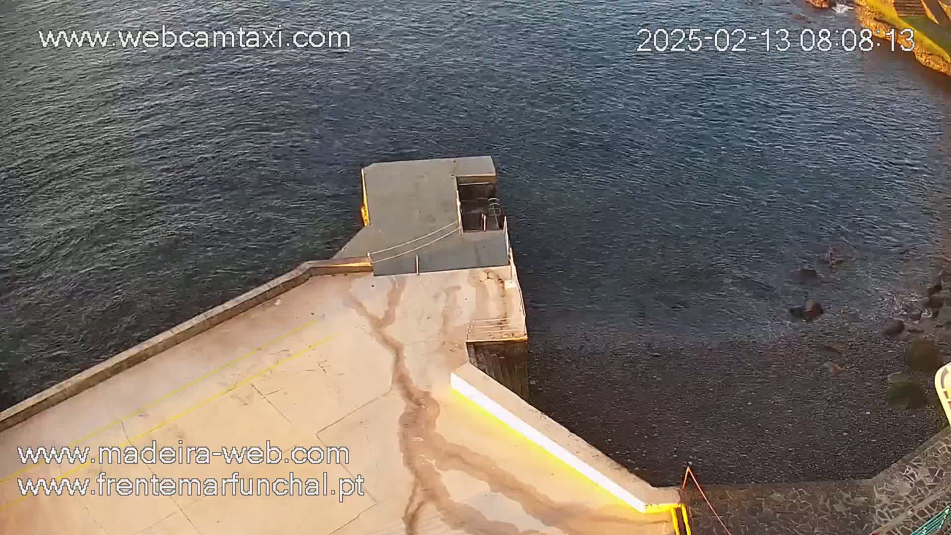 A high-angle view shows a concrete platform extending over dark water, with a small dock at the end.