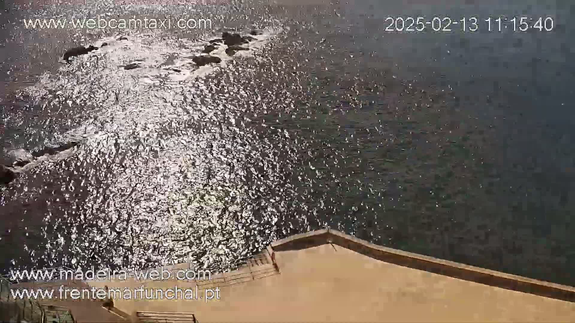 Sparkling water laps against a tan concrete wall on a sunny day.