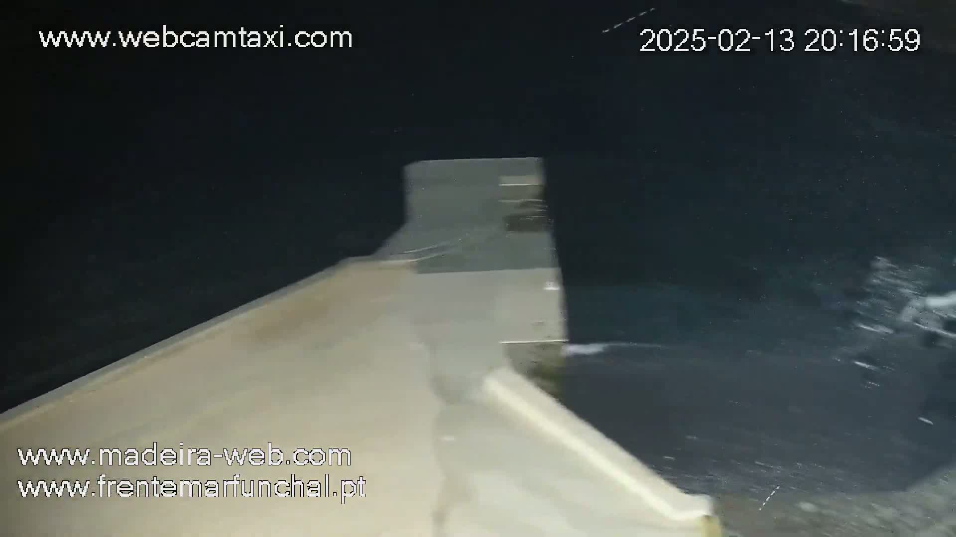 A nighttime, low-angle view shows dark water splashing against a light-colored concrete structure.