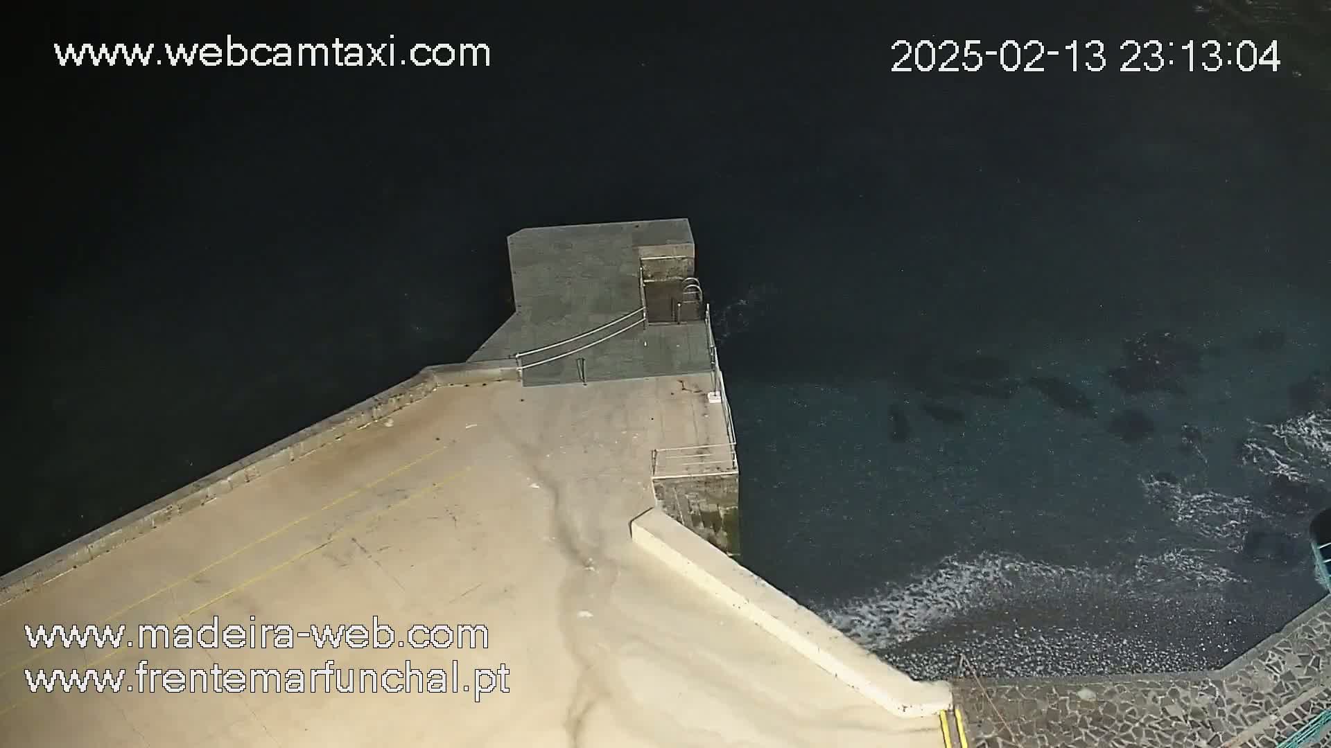 A nighttime, high-angle view shows a concrete platform extending into dark water with small waves lapping against its edge.