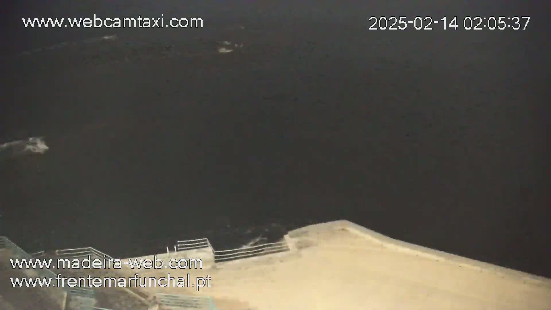 A nighttime view of dark water with small waves crashing against a light-colored wall.