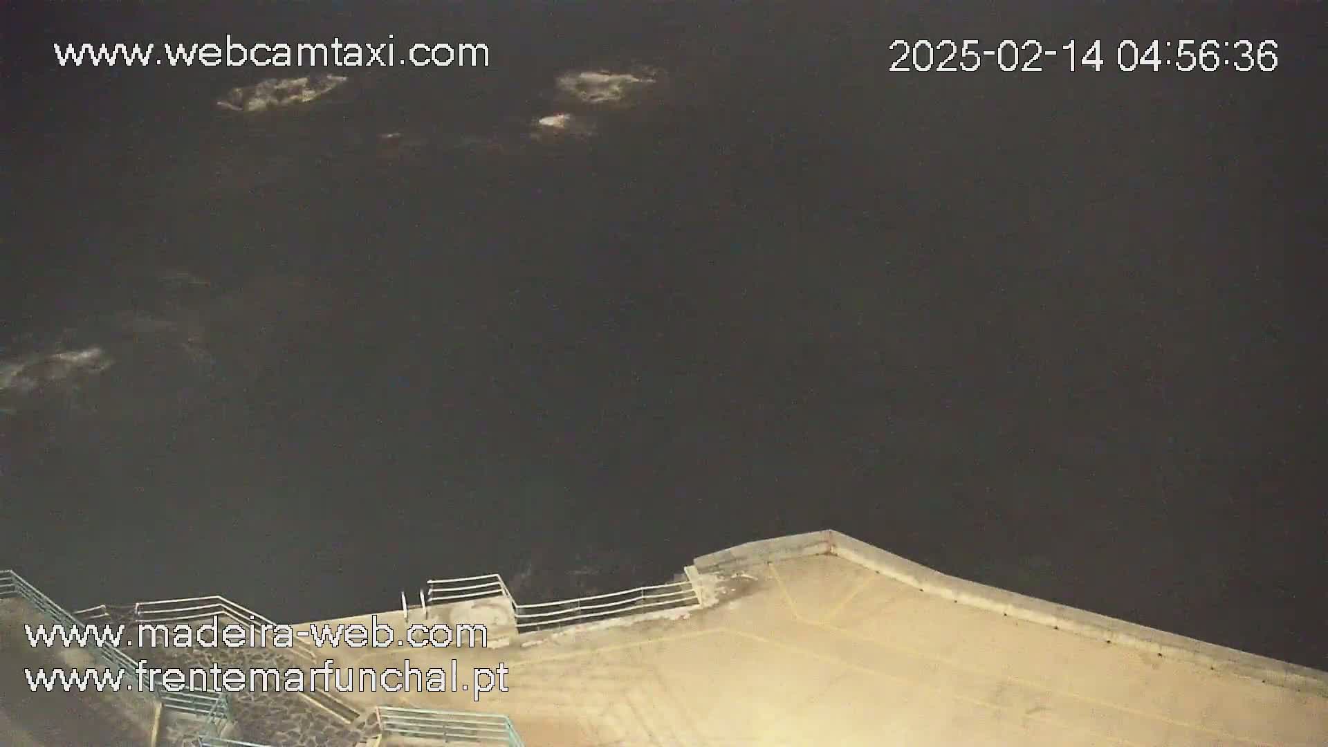 A nighttime, high-angle view shows a dark body of water lapping against a concrete embankment.