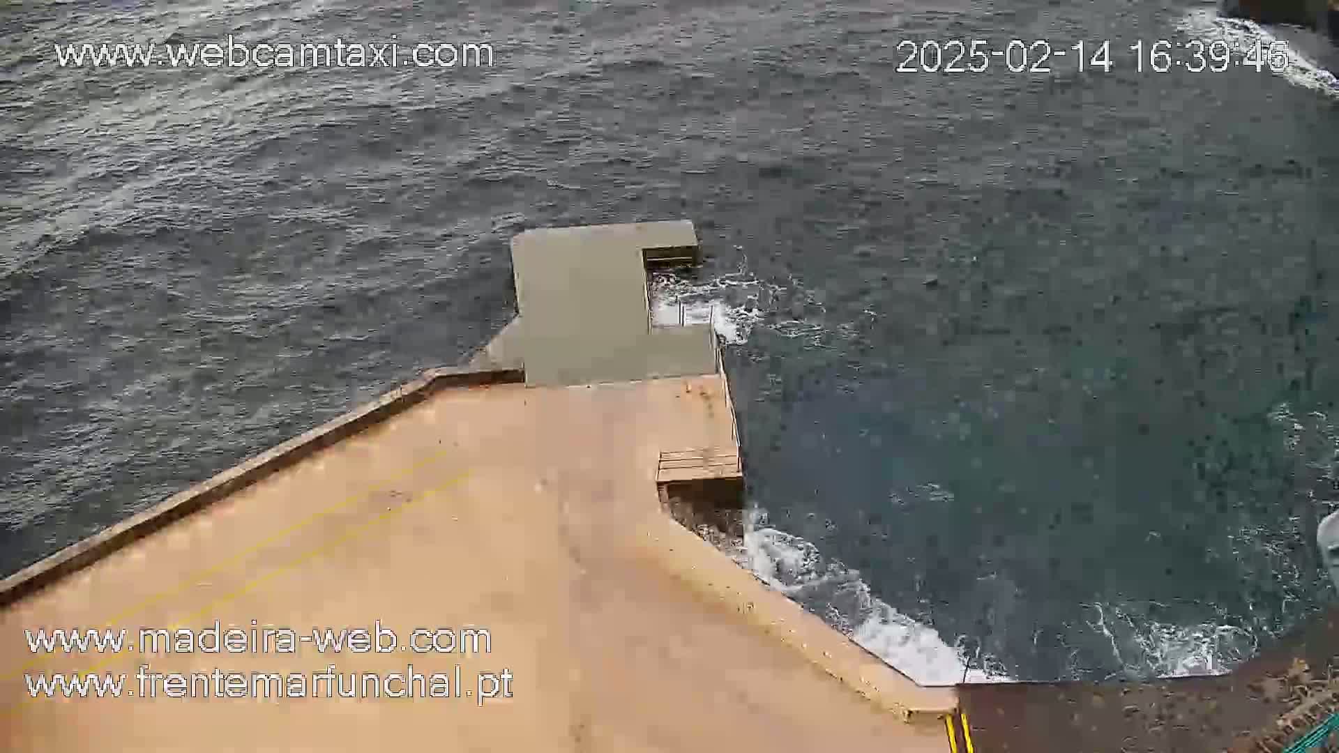 A tan concrete structure extends from a rocky shoreline into a dark, choppy ocean.