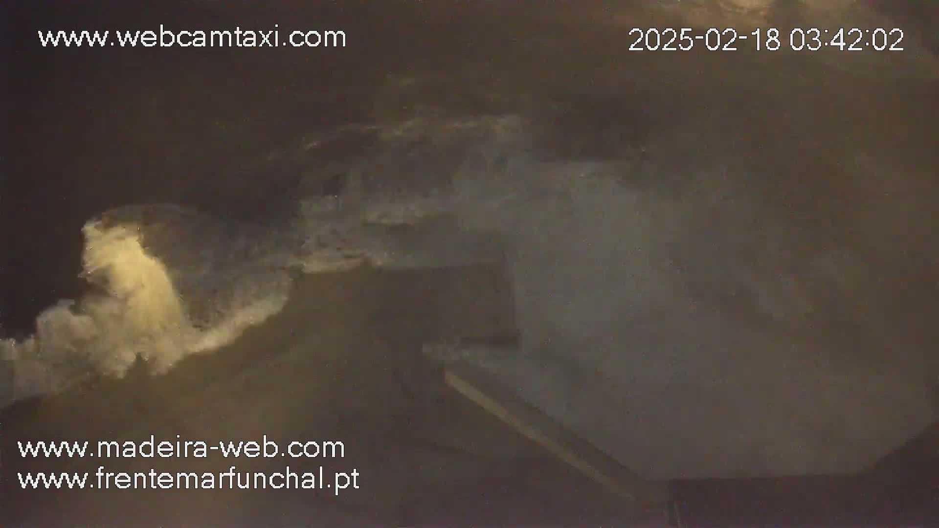 Large waves crash against a structure at night.