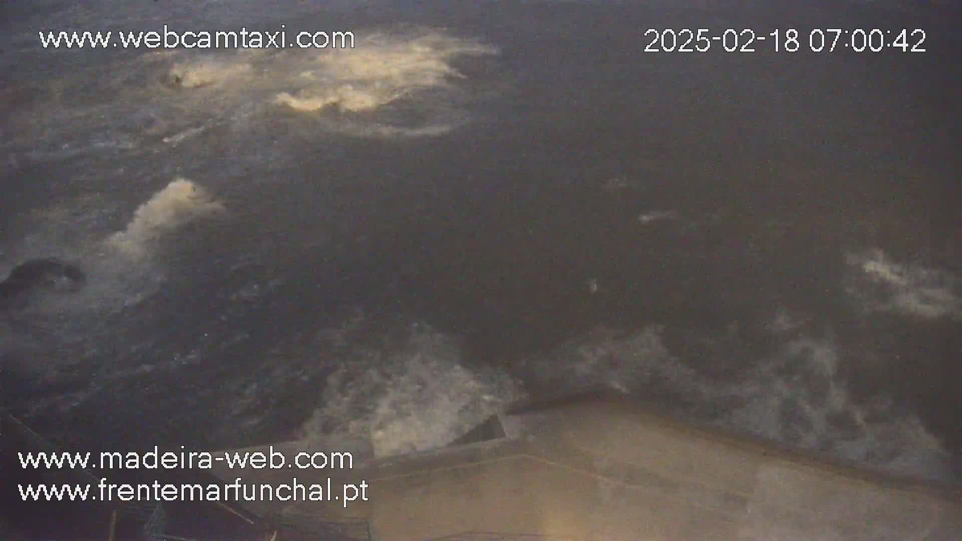 A dark-grey body of water with white, foamy patches and waves is seen from an elevated angle.
