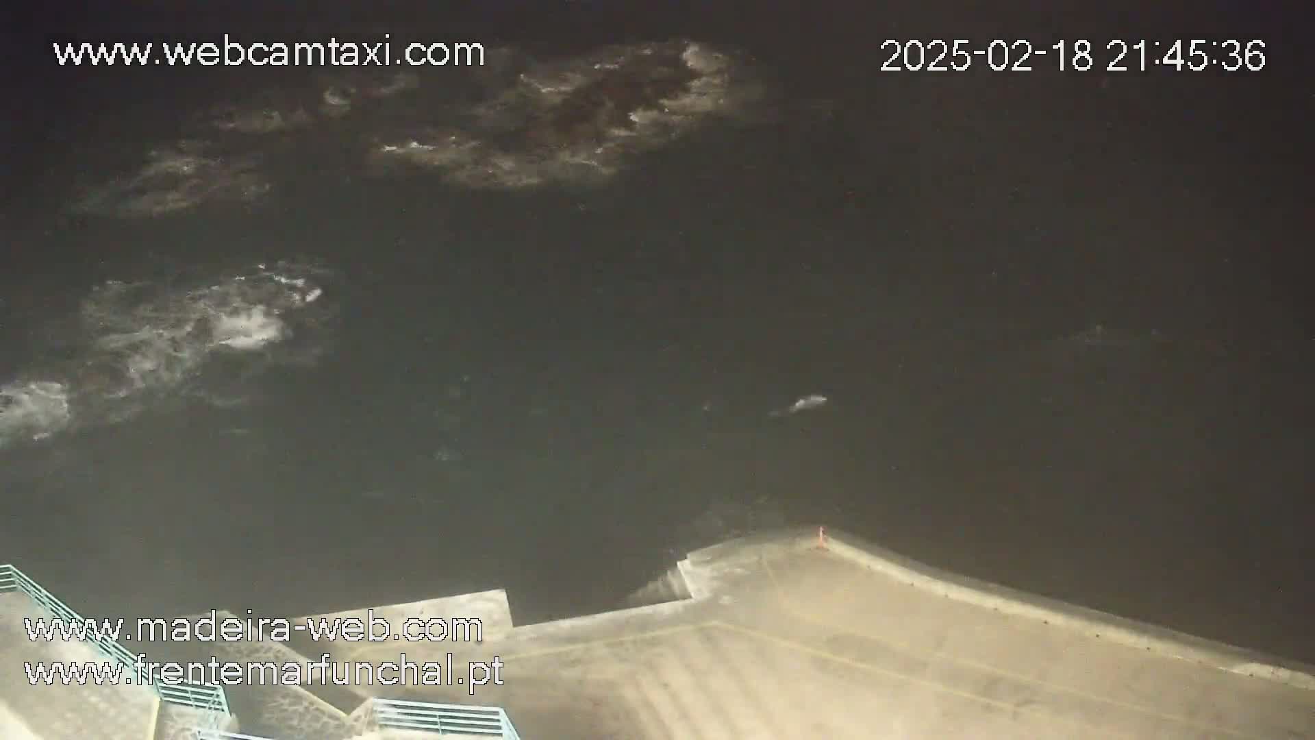 A nighttime view of dark water with some whitecaps near a concrete structure under a mostly clear, dark sky.