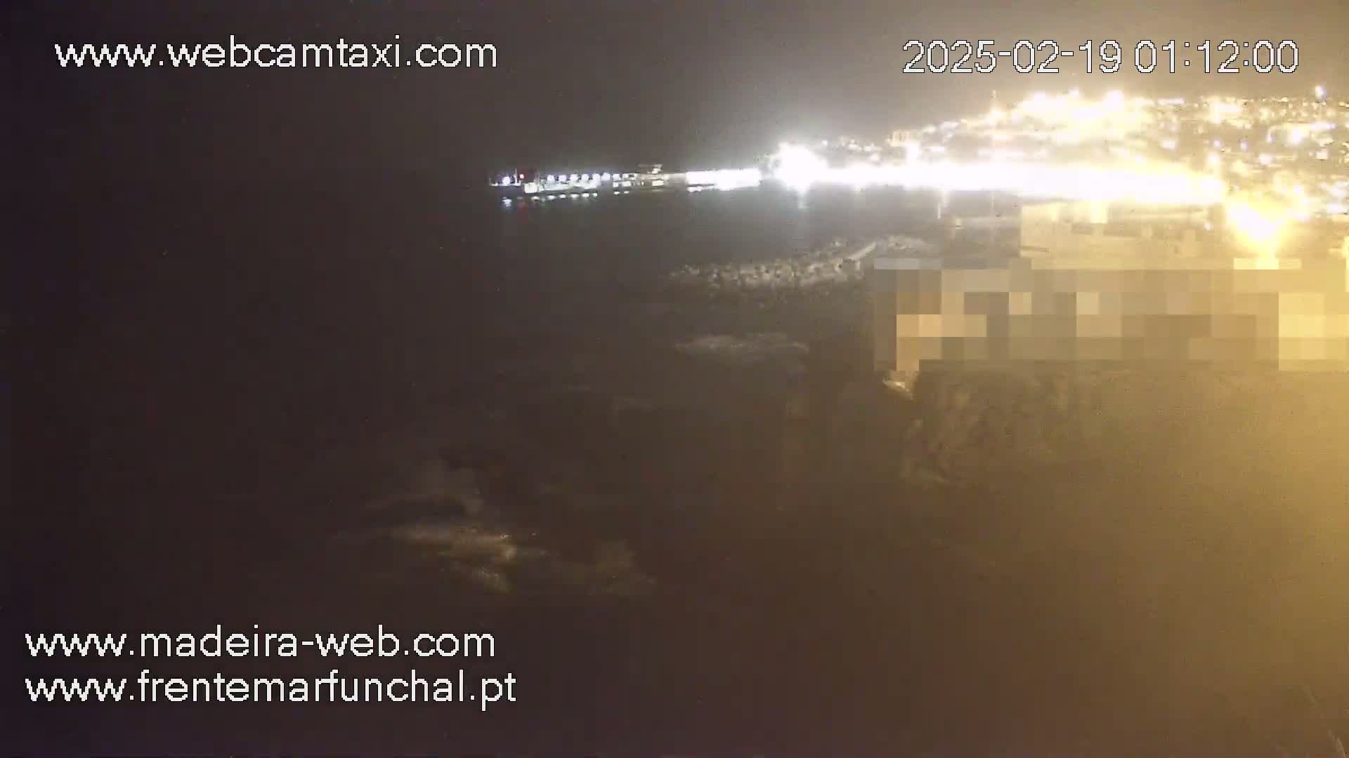 A nighttime, hazy view of a coastline with brightly lit buildings and a body of water in the distance.