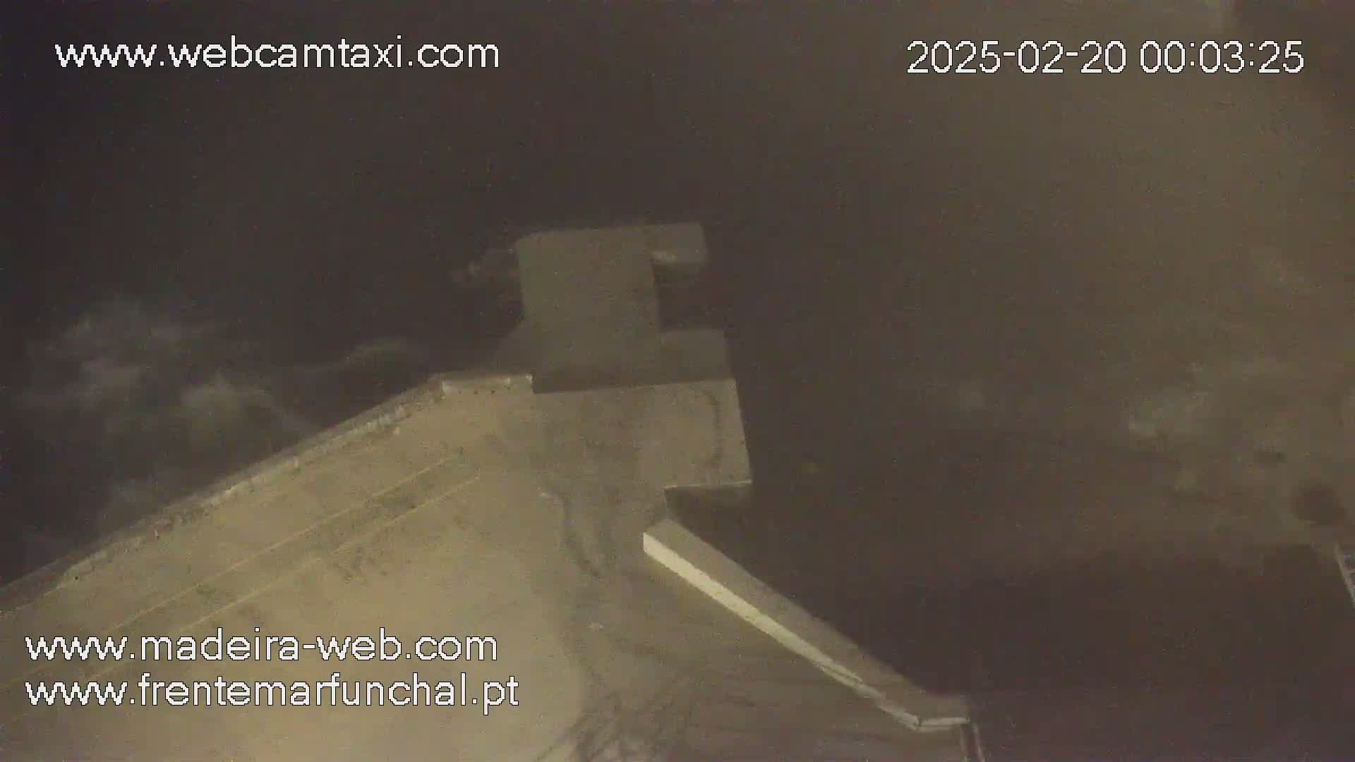A nighttime, slightly cloudy view of a tan-colored building, possibly a wall or structure, extending from the bottom to the middle of the frame.