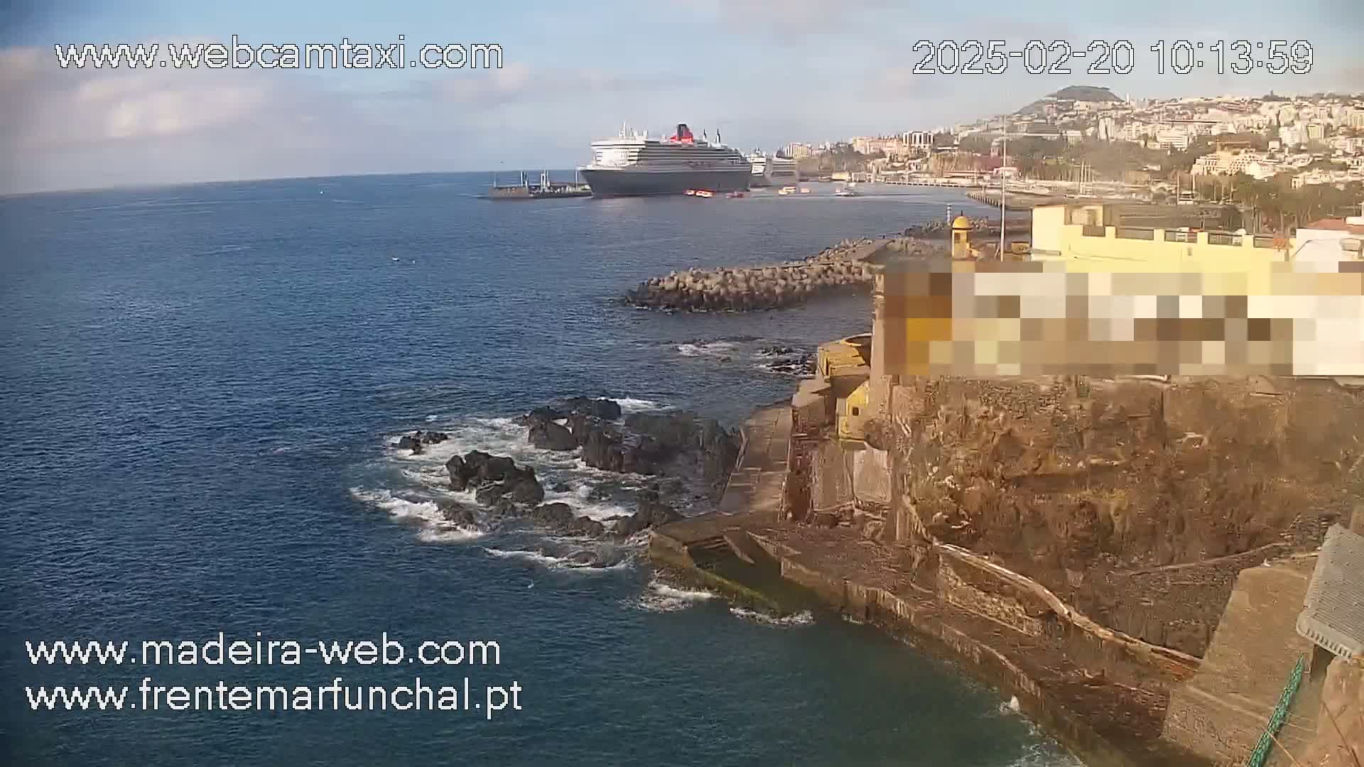 A large cruise ship is docked near a rocky coastline on a partly sunny day.