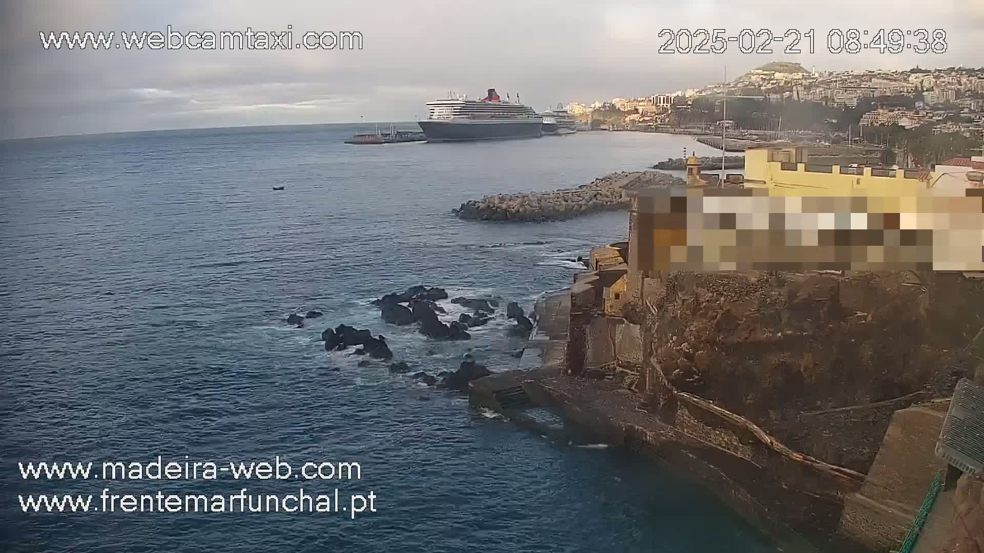 A large cruise ship is docked in a harbor near a rocky coastline under an overcast sky.
