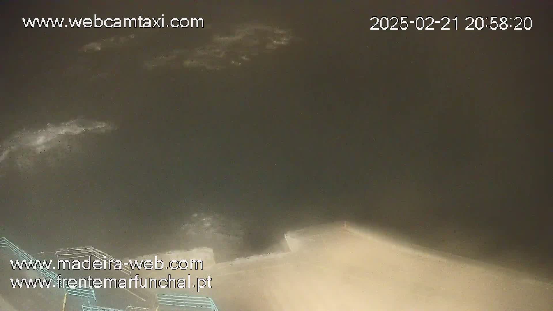 A nighttime, hazy view shows a dark body of water with some whitecaps and a light-colored structure at the bottom of the frame.