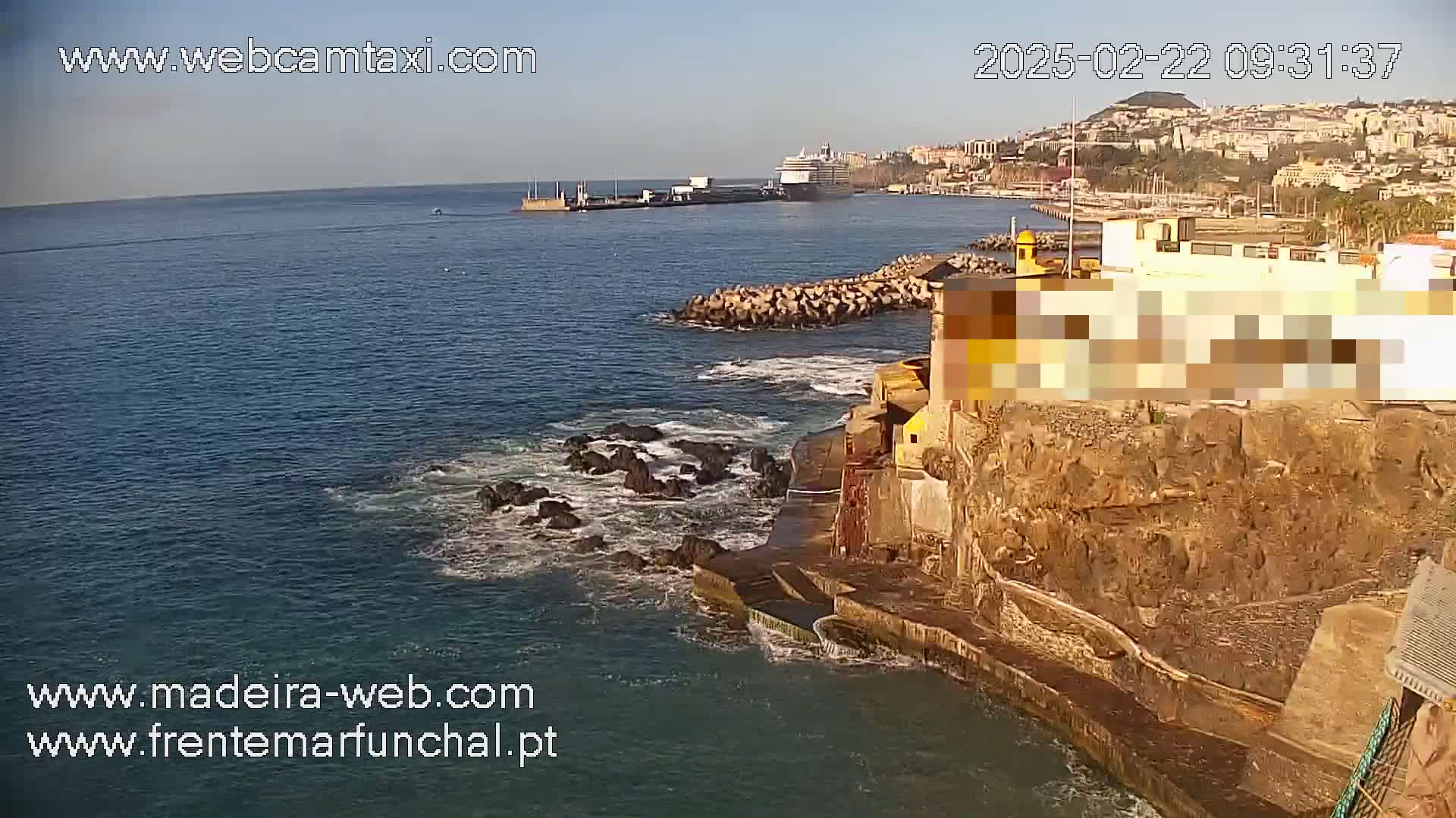 A cruise ship is docked in a harbor next to a rocky coastline on a sunny day with calm water.