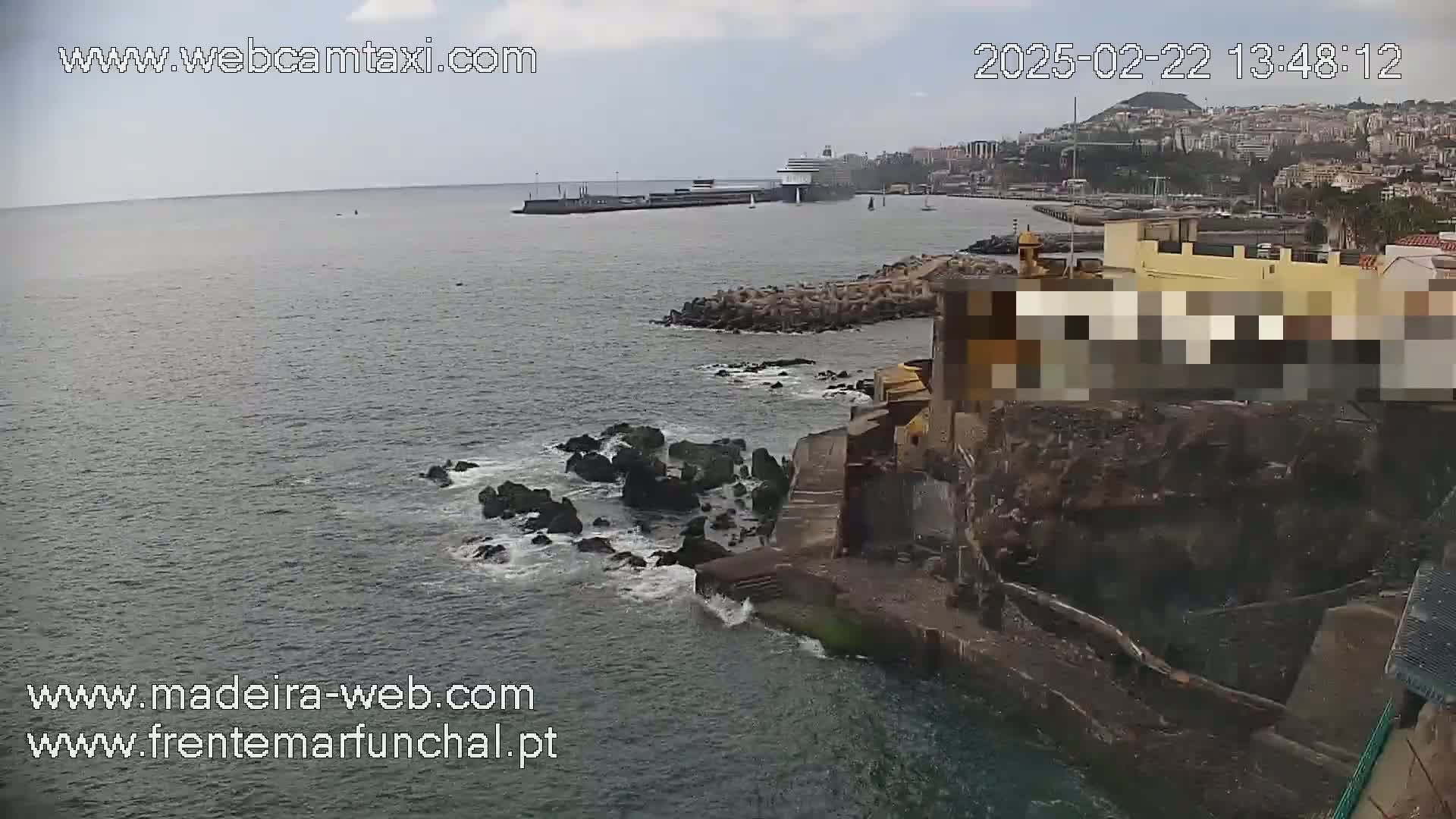 A cruise ship is docked in a harbor next to a rocky coastline, under an overcast sky.