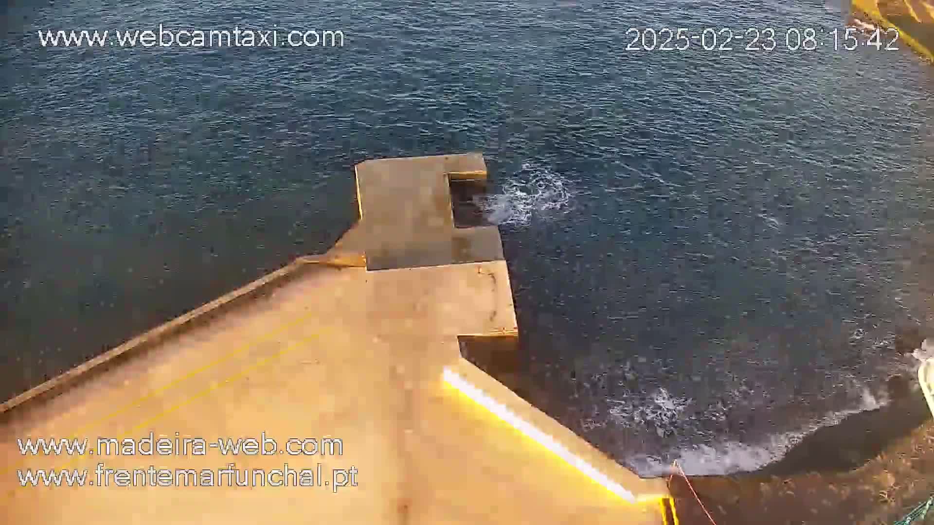 A concrete pier extends over dark-blue water with small waves lapping against its edge, lit by a long, bright light.
