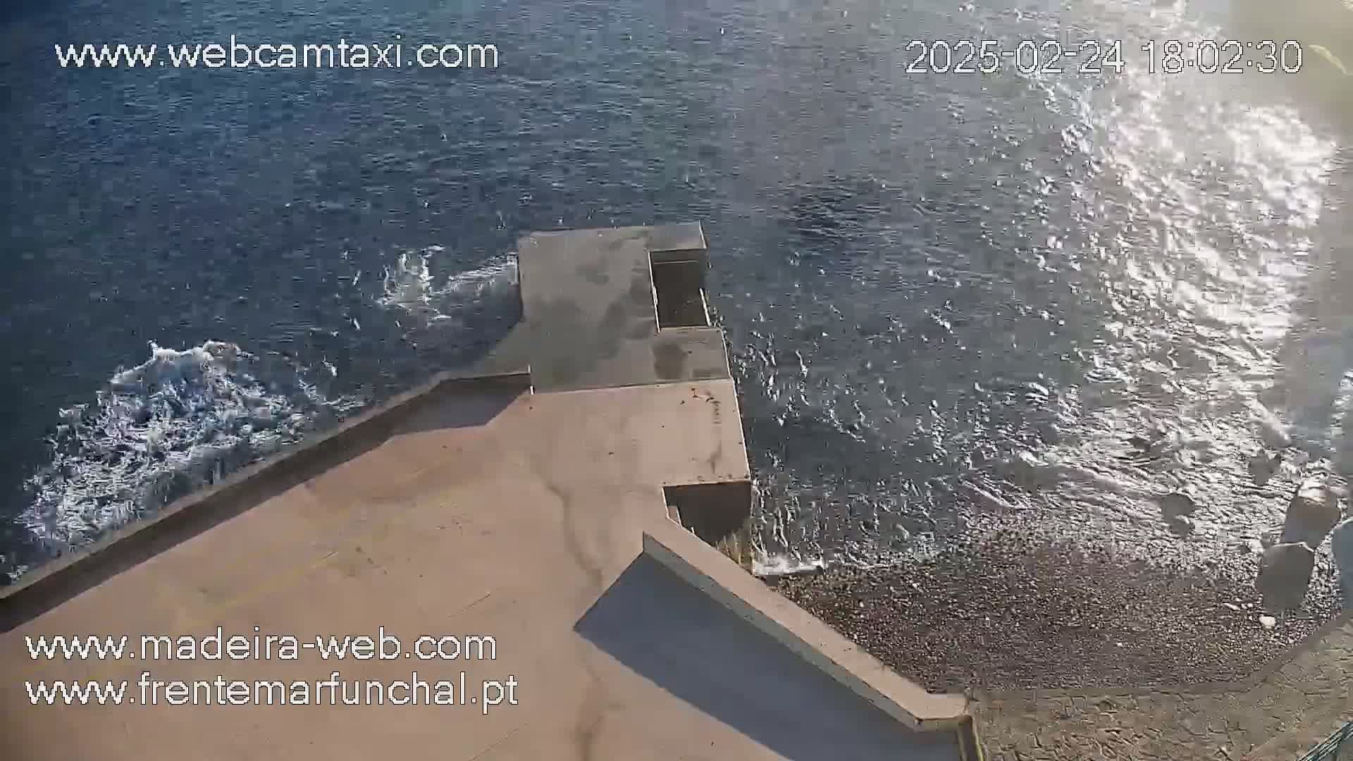 A rocky shoreline with a concrete structure meets a dark-blue sea with small waves.