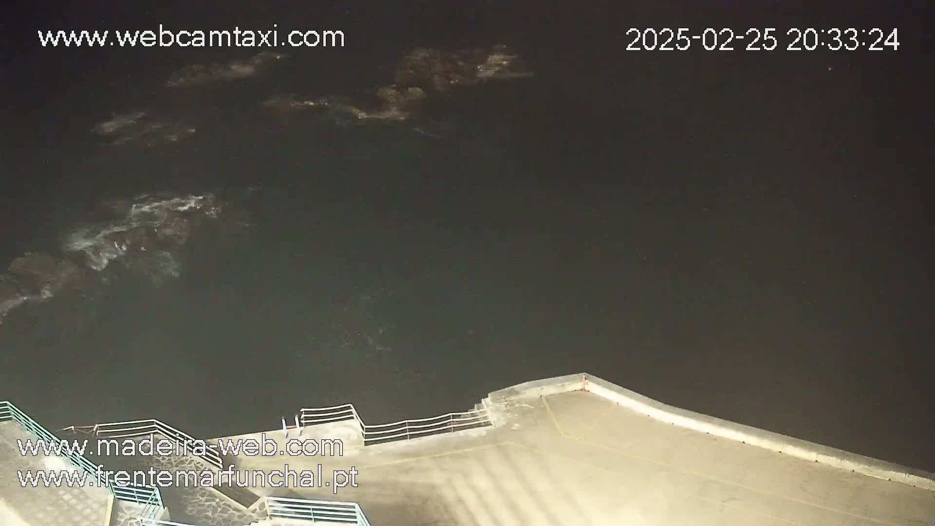 A nighttime, high-angle view shows dark water with some small waves lapping against a concrete structure with a railing.