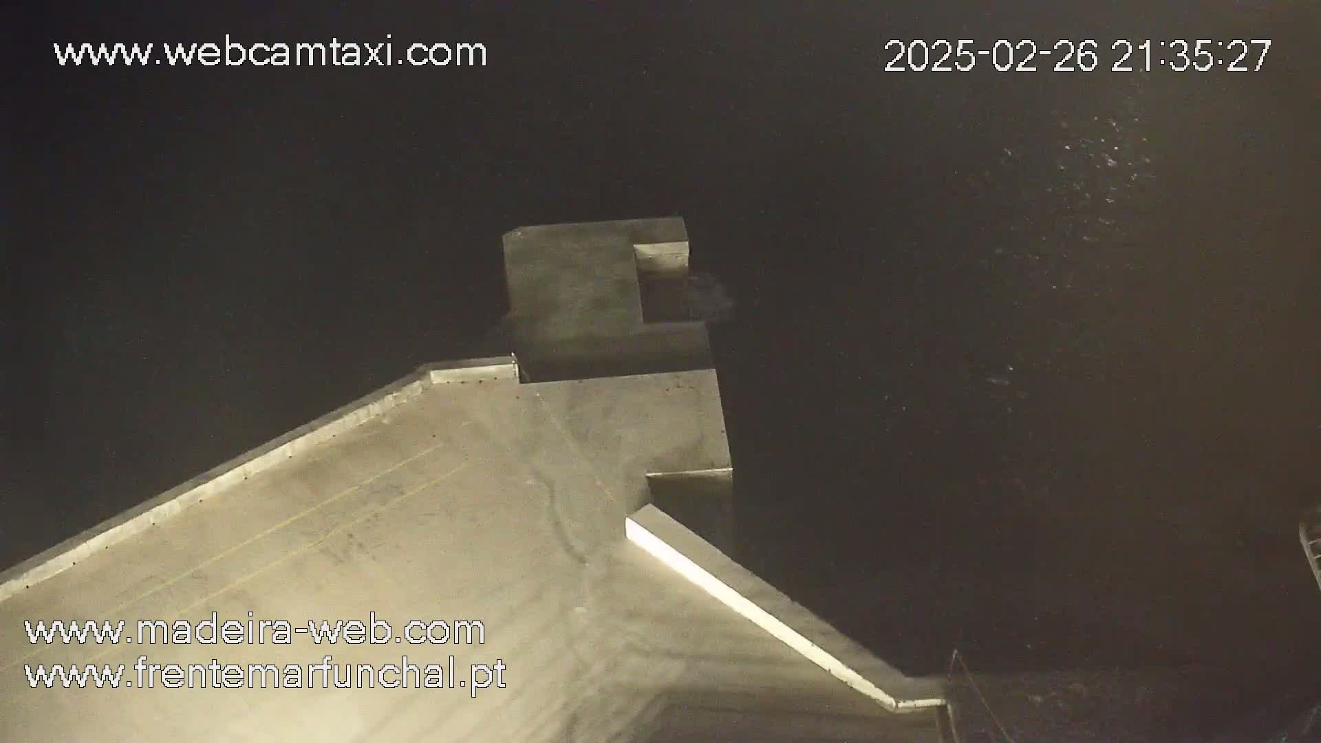 A high-angle nighttime view shows a concrete structure extending into dark water.