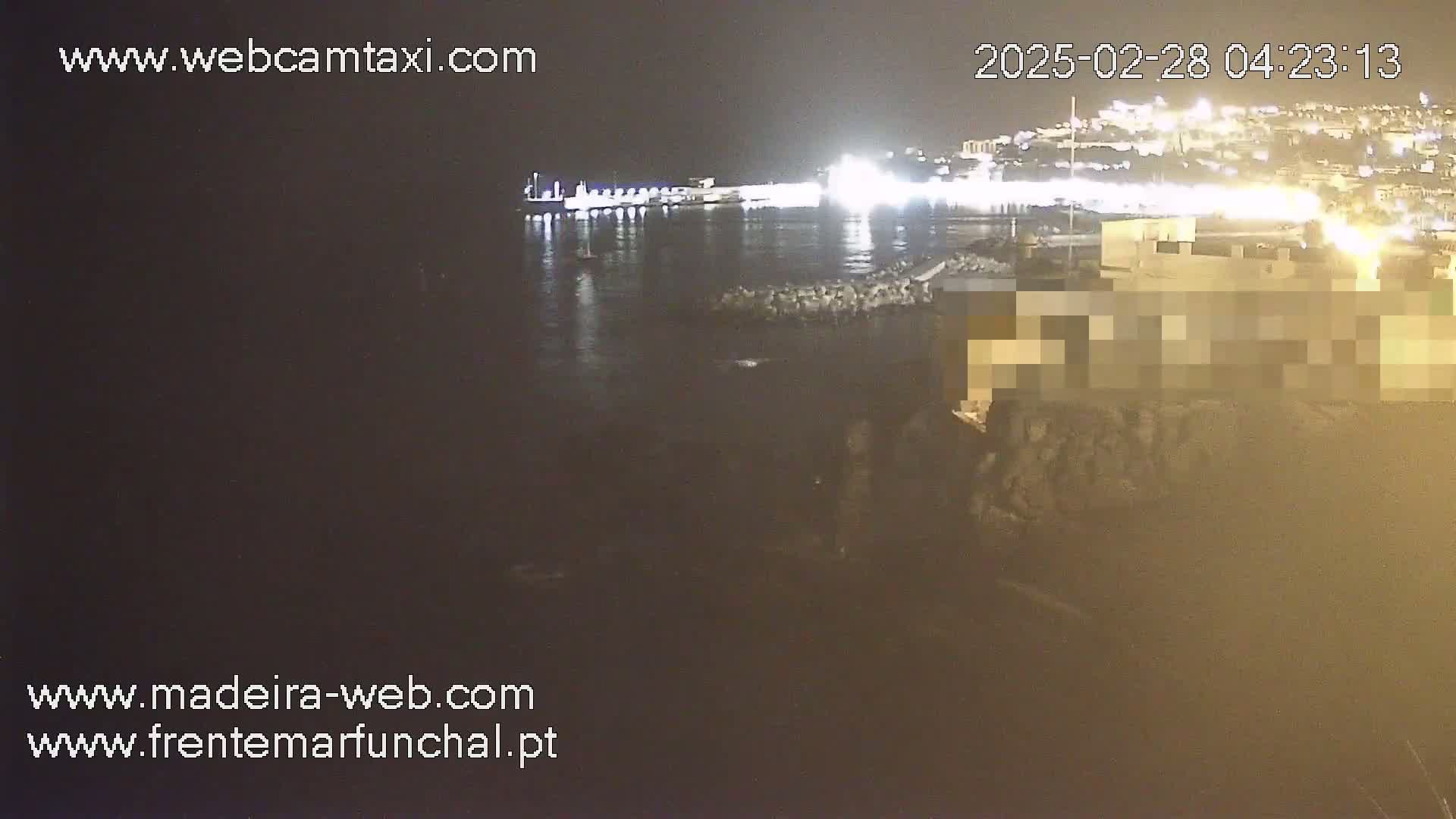 A nighttime, seaside view shows a dark body of water reflecting the lights of a distant city.