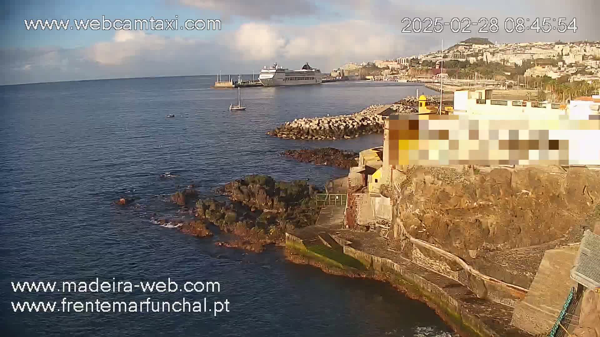 A large cruise ship is docked near a rocky coastline under partly cloudy skies.