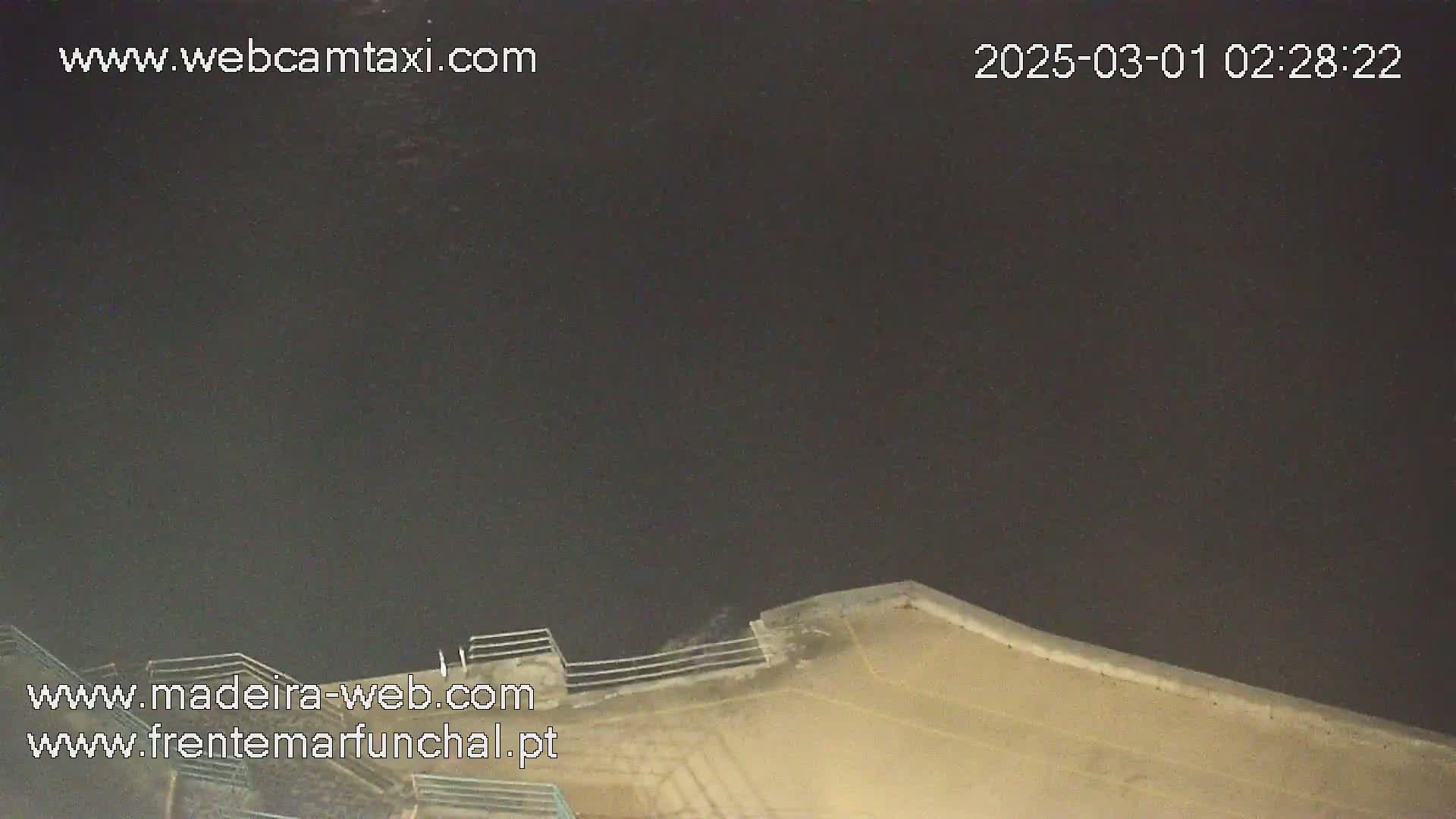 A nighttime, dark view of a concrete structure with a railing, possibly a seawall or rooftop, under a clear, dark sky.