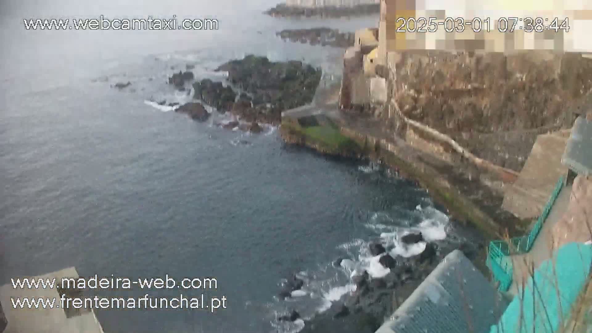 A rocky coastline with a stone structure meets a choppy, gray sea under an overcast sky.