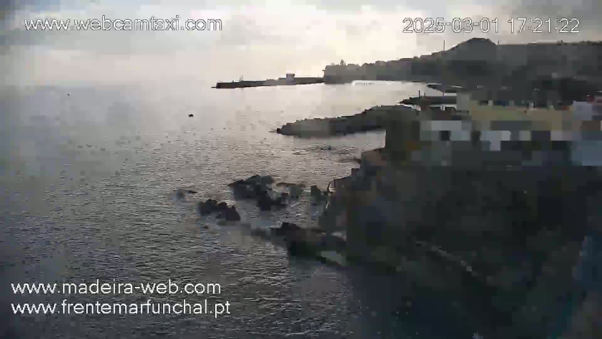 A coastal town is seen on a slightly overcast day, with dark-colored water lapping against rocky shores.