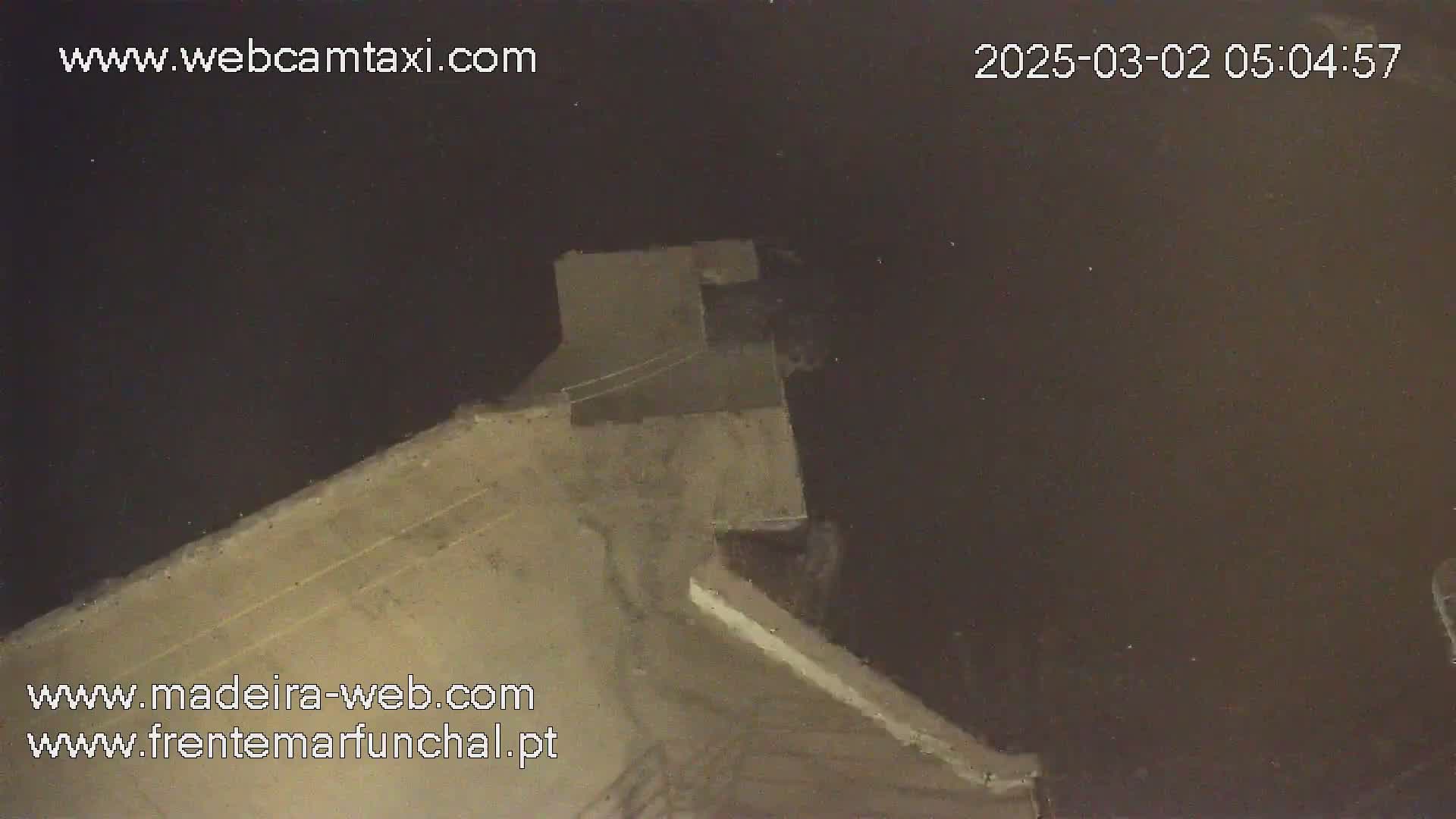 A high-angle, nighttime view shows a light-tan concrete structure extending into dark water.