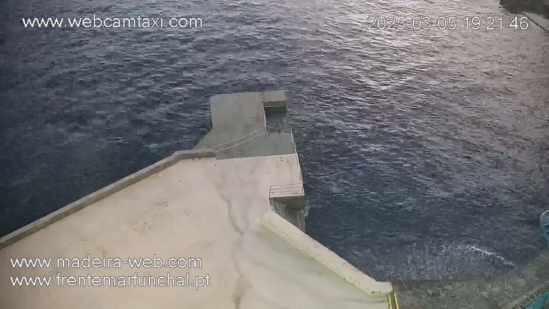 A high-angle view shows a concrete structure extending into a dark, choppy body of water.
