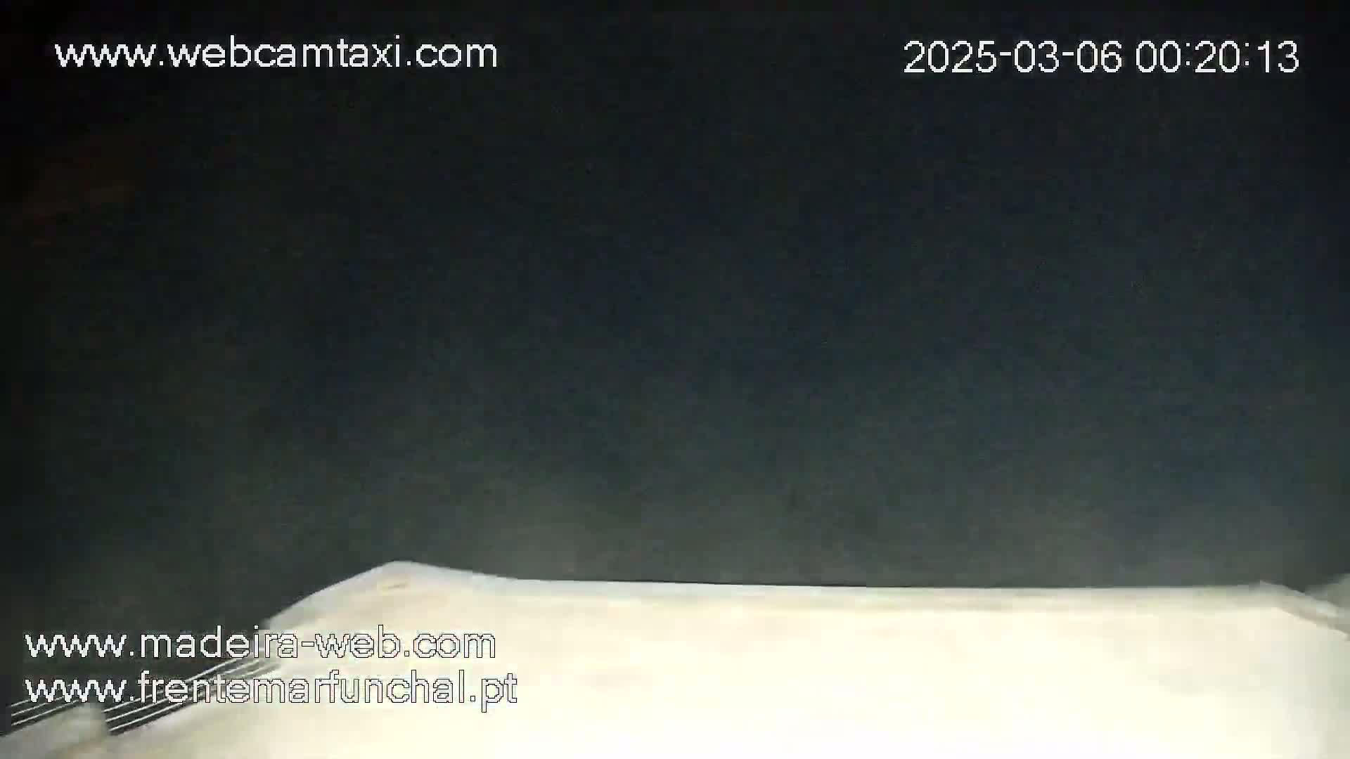 A nighttime, low-angle view shows the top of a white surface, possibly a car hood, against a dark background.